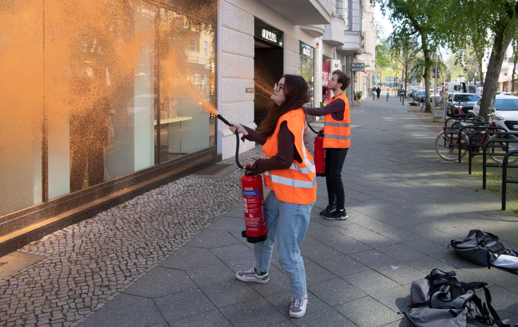 22 April 2023, Berlin: Activists from the environmental group Letzte Generation spray a facade of a luxury store. "The richest Germans emit a thousand times as many greenhouse gases as the average. While the ordinary people have to bear the consequences, a few can buy their way out of the catastrophic consequences of the climate catastrophe, which they have played a major role in causing, for a long time to come," said a statement from Last Generation about the protest action. (Paul Zinken/picture alliance—Getty Images)