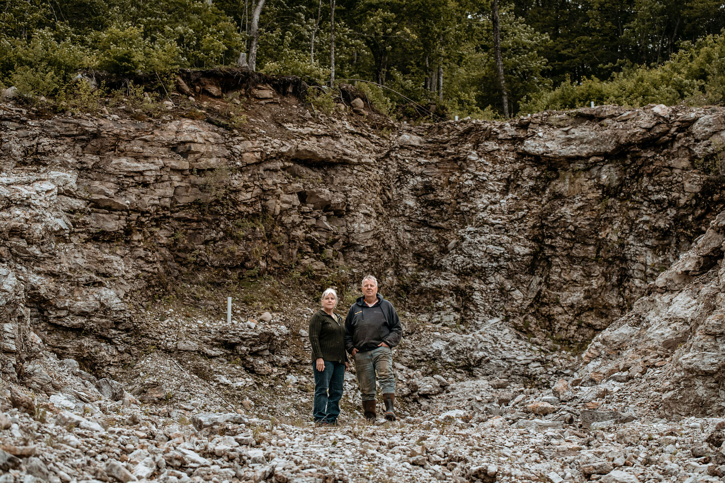 Mary and Gary Freeman stand in a pit in Newry, Maine, where they have excavated 700 tons of the lithium-bearing mineral spodumene under an exploratory permit, on June 6. The site, also known as Plumbago North, contains some of the largest specimens of  spodumene ever uncovered, with some measuring up to 36 feet in length. The state of Maine currently bars them from further extracting the rock. (Garrick Hoffman—The Maine Monitor)