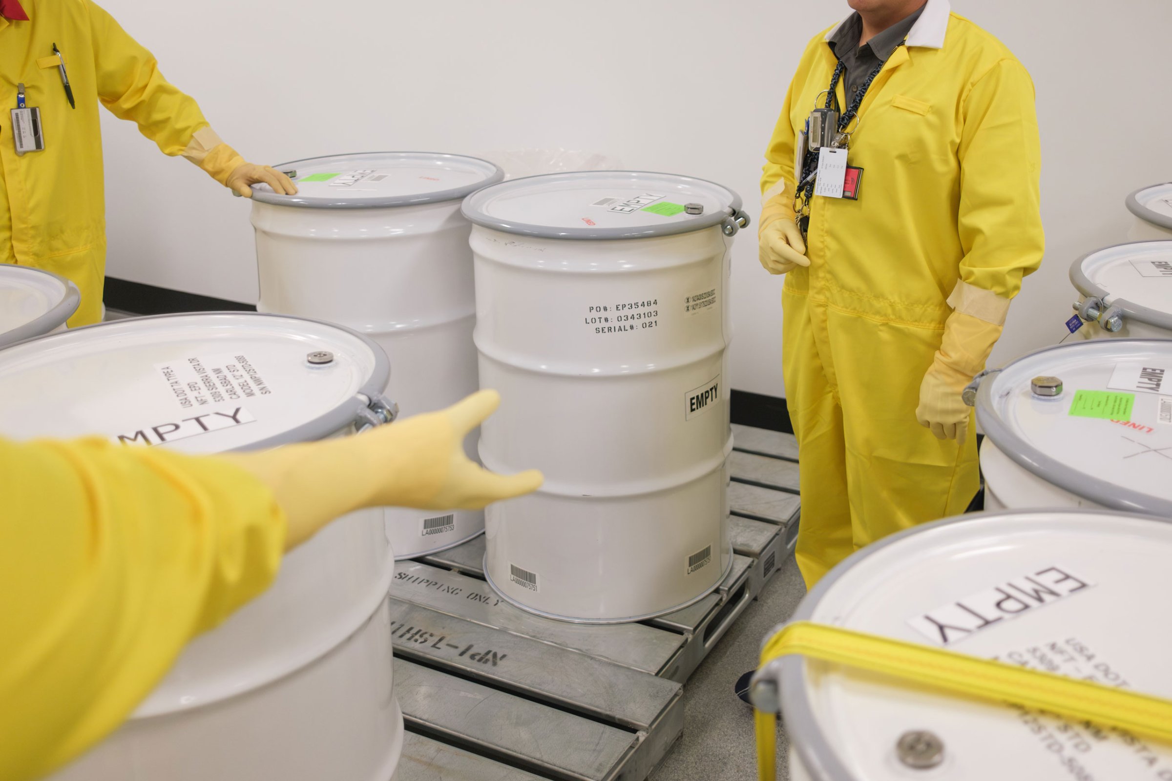 lab employees wearing yellow suits stand by empty waste drums used for training