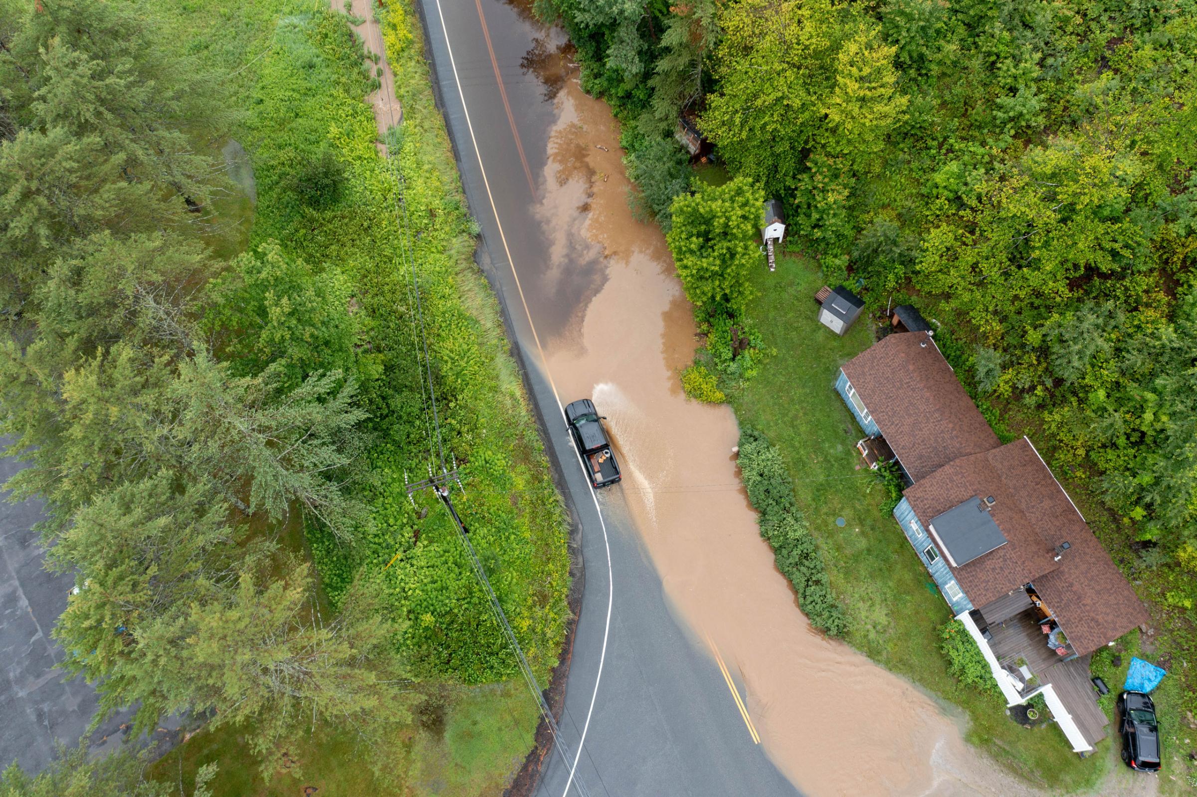 In an aerial view, a pick-up truck drives along a flooded road after heavy rain