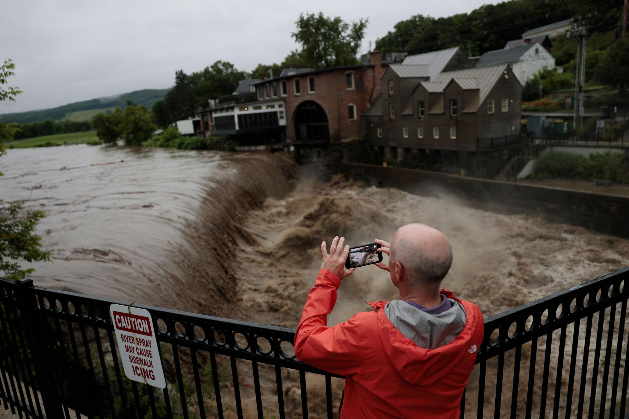 A man stops to take a photo as heavy rain sends mud and debris down the Ottauquechee River