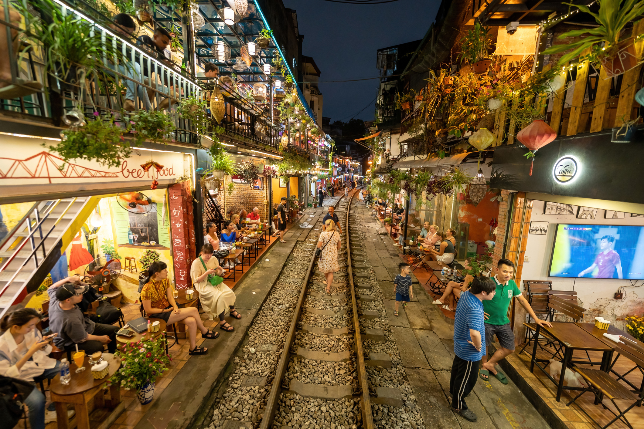 View of train passing through a narrow street of the Hanoi Old Quarter. Tourists taking pictures of hurtling train. The Hanoi Train Street is a popular attraction.