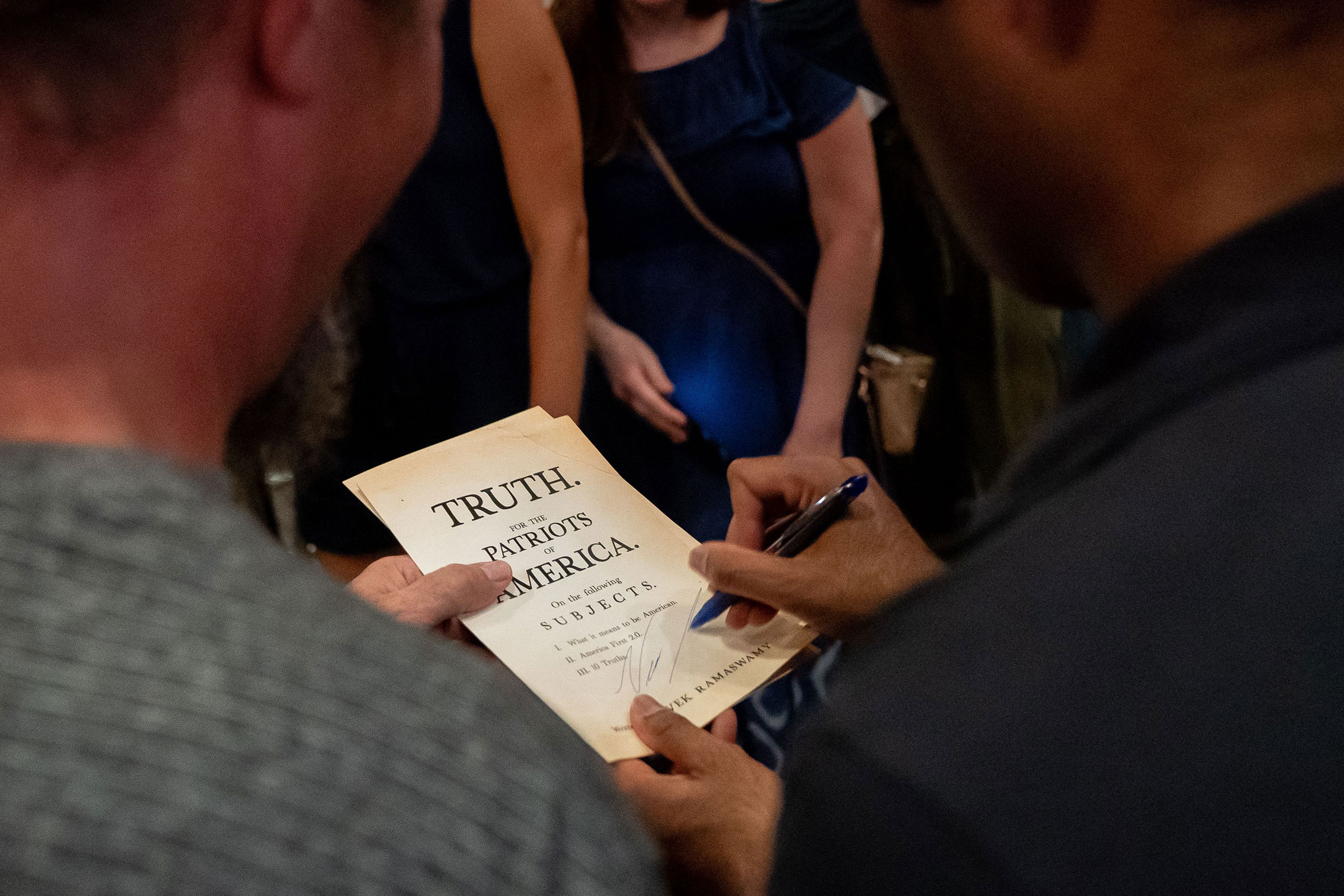 Ramaswamy signs a pamphlet with a pen that says "truth. for the patriots of america" on it