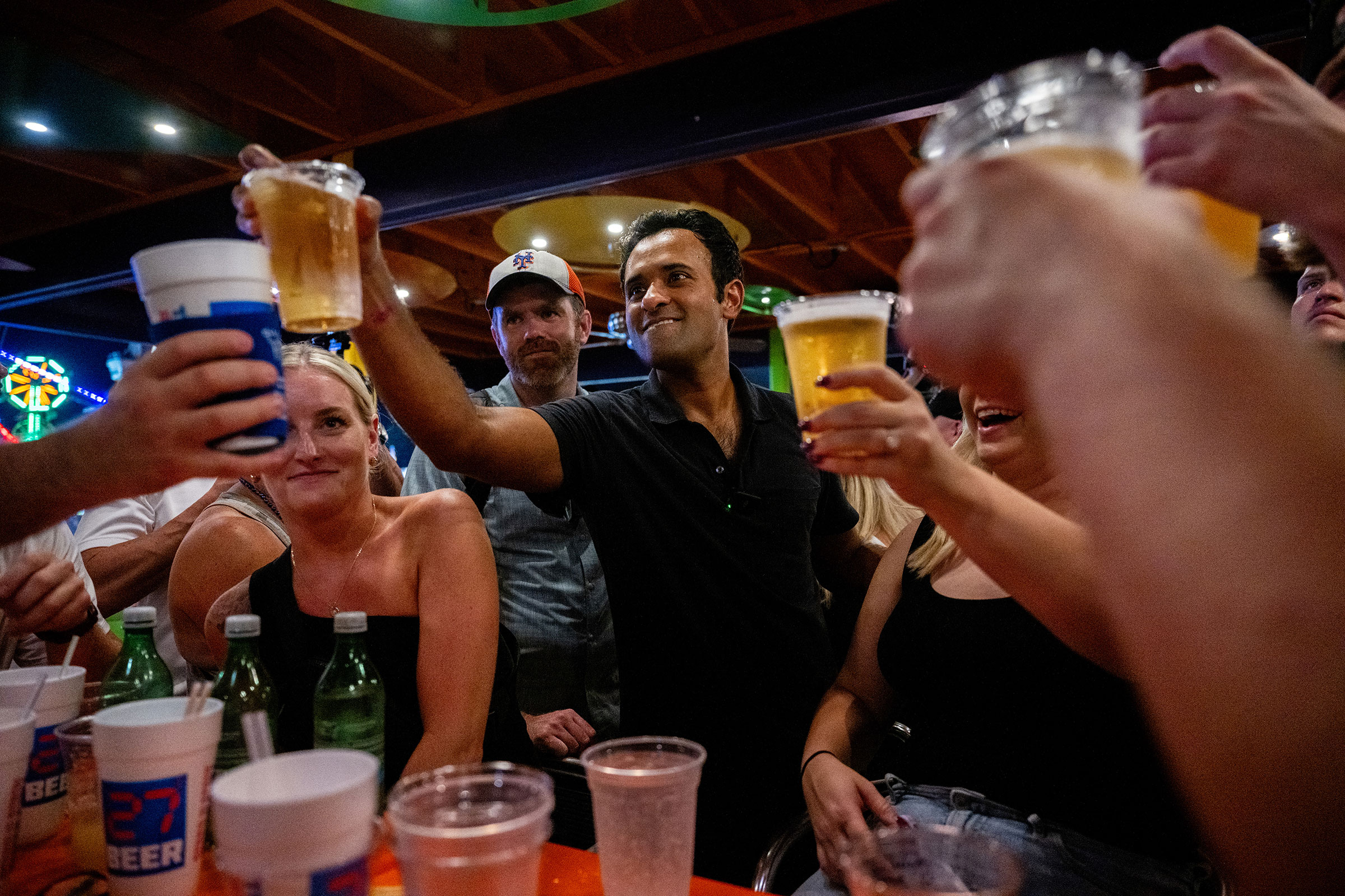 Vivek Ramaswamy holds a beer in the air as he toasts with supporters in a bar