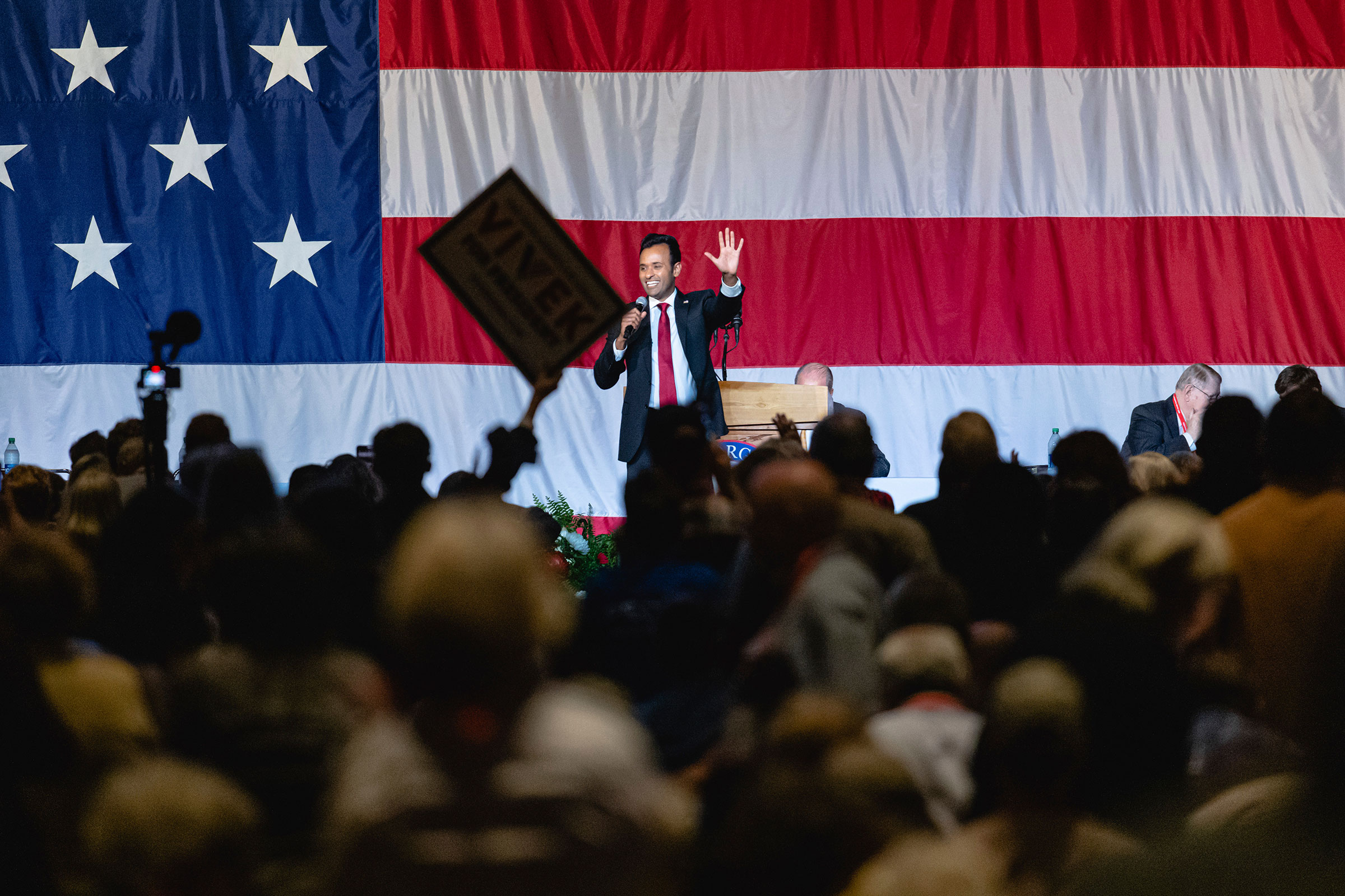 Vivek Ramaswamy, a Republican presidential candidate and businessman, waves toward the audience as he stands on a stage with the American flag behind him