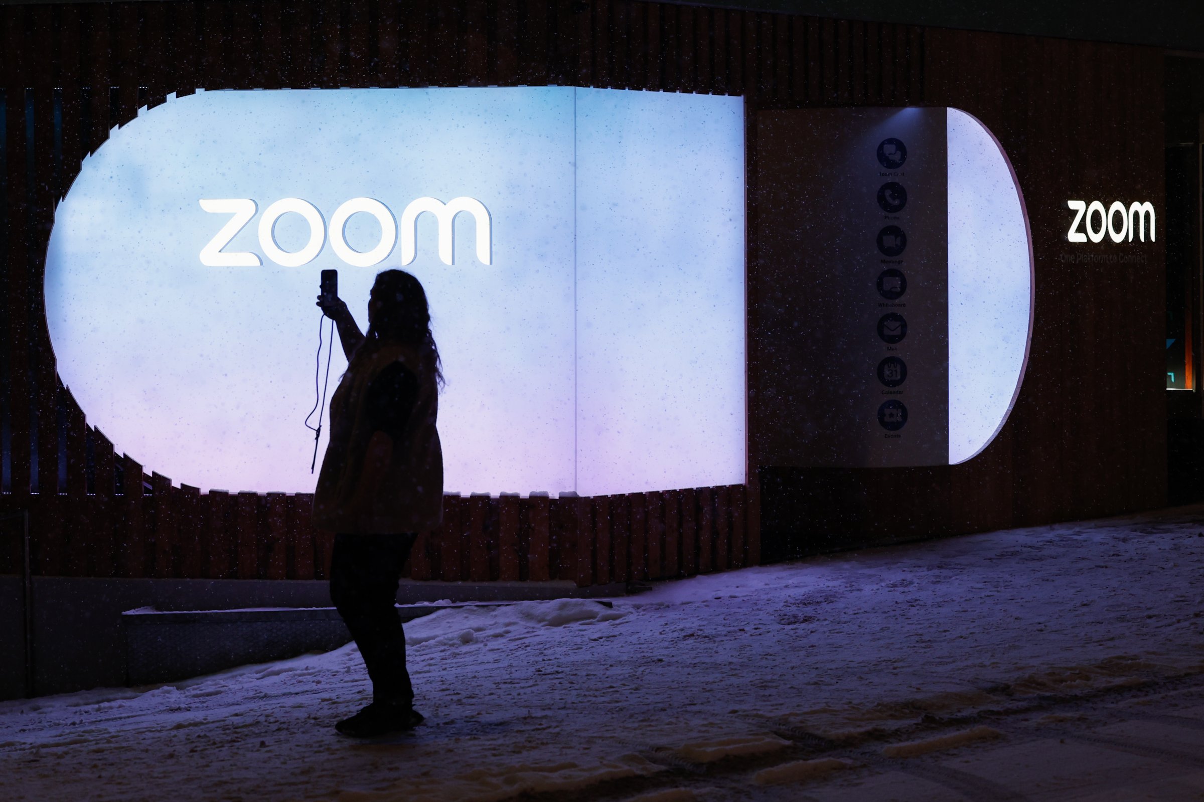 A silhouetted person poses in front of a Zoom sign