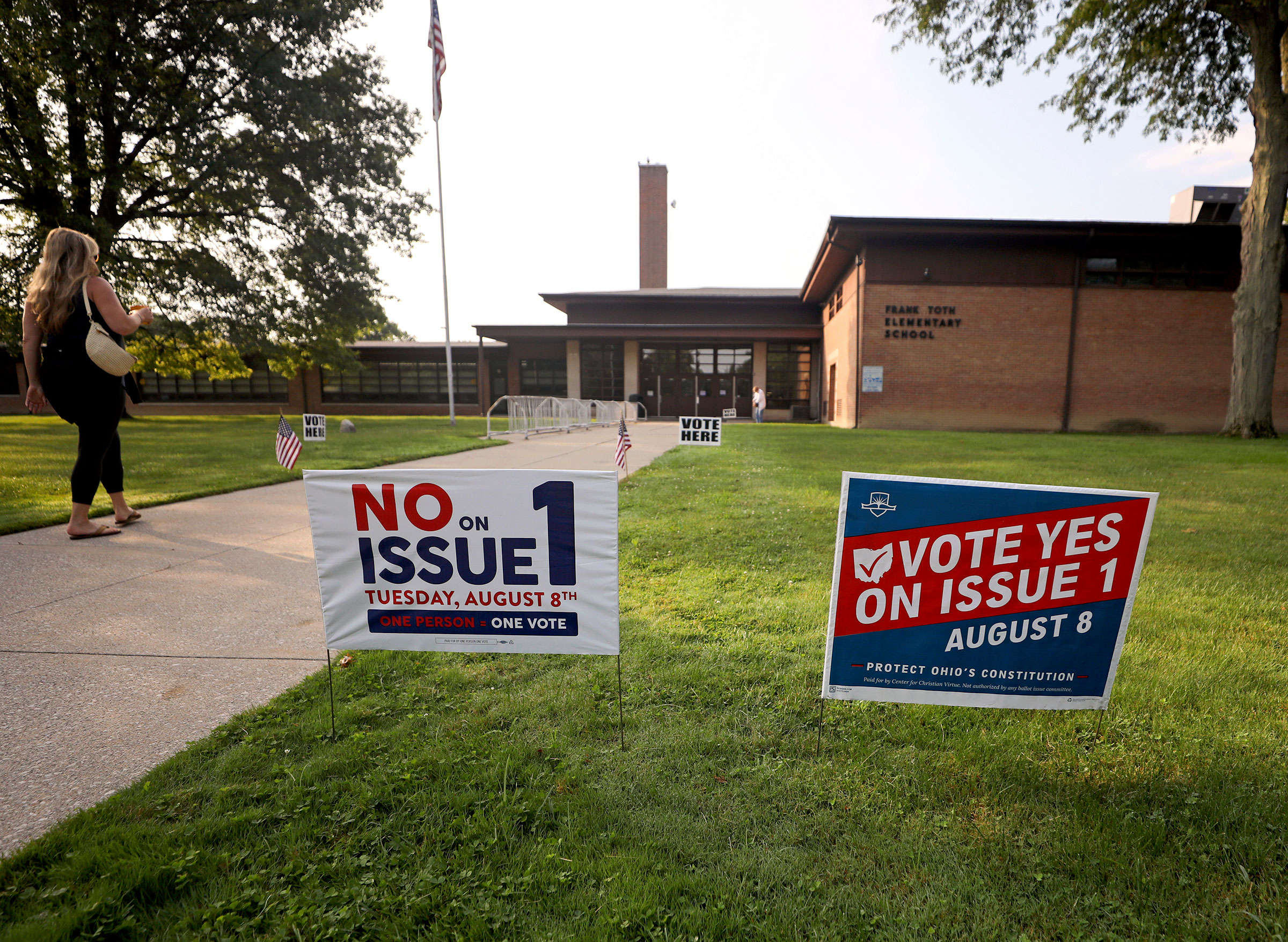 Two opposing signs with slogans posted in the green grass in front of an elementary school where people are going in to vote