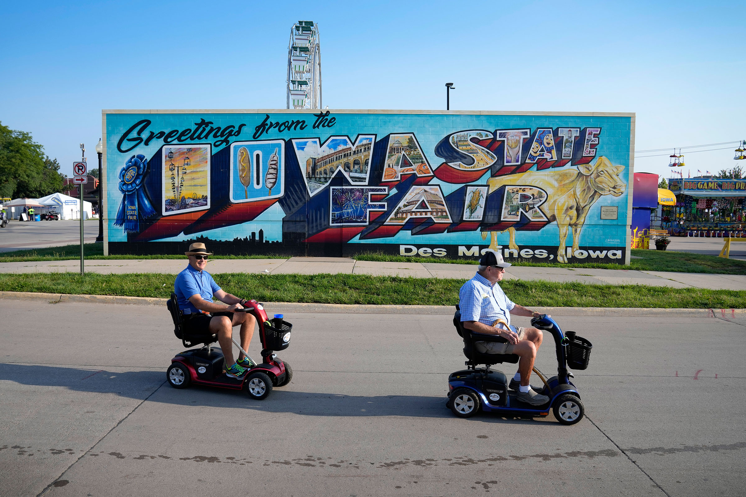 Two men ride scooters across the parking lot in front of Iowa State Fair sign