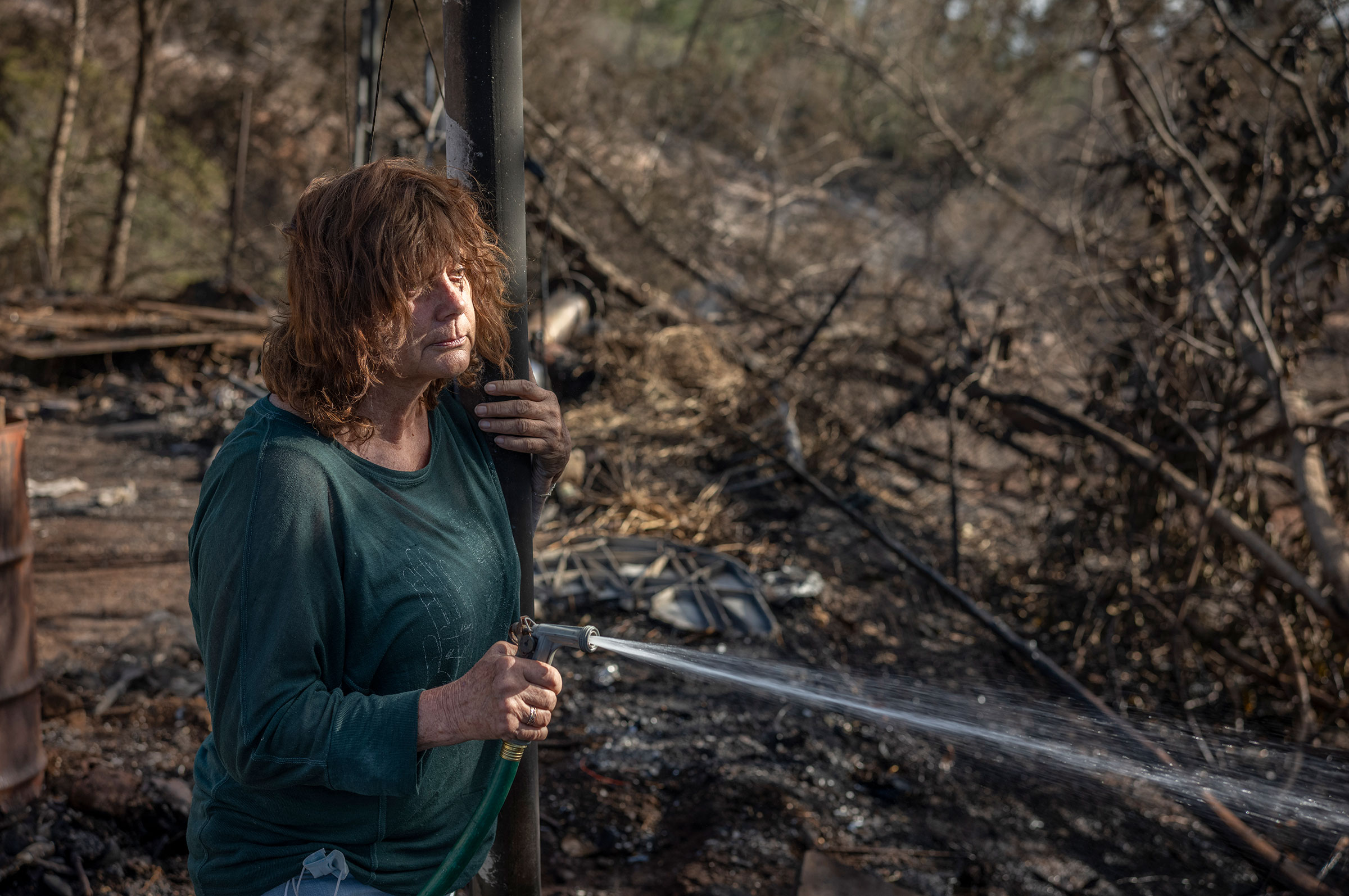 A woman, who asked not to be named, hoses down a still-hot part of the property of a friend whose house burned down in Kula on Aug. 12. (David Butow for TIME)