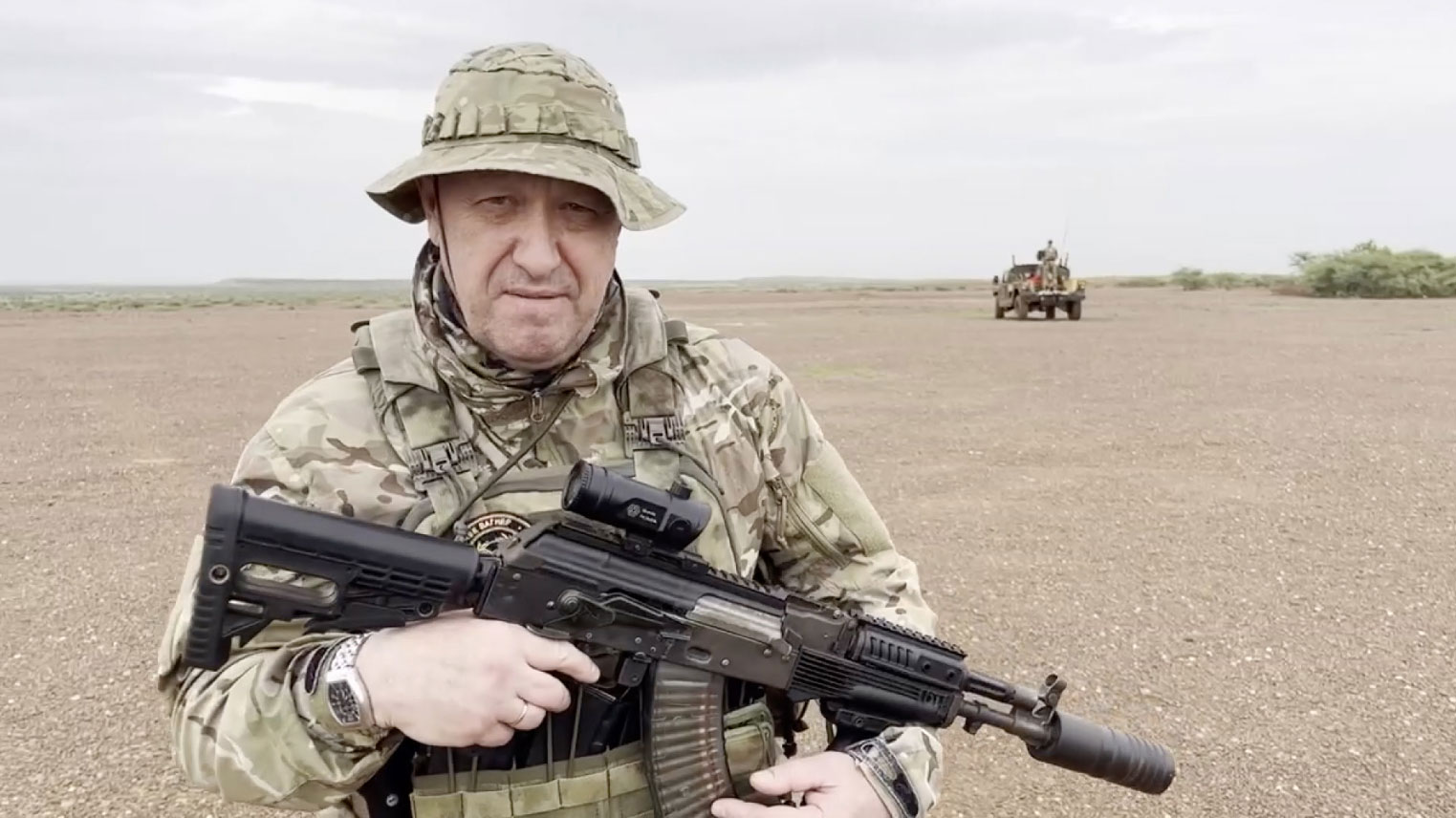 video screenshot of Yevgeny Prigozhin holding a rifle in a desert area while wearing camouflage