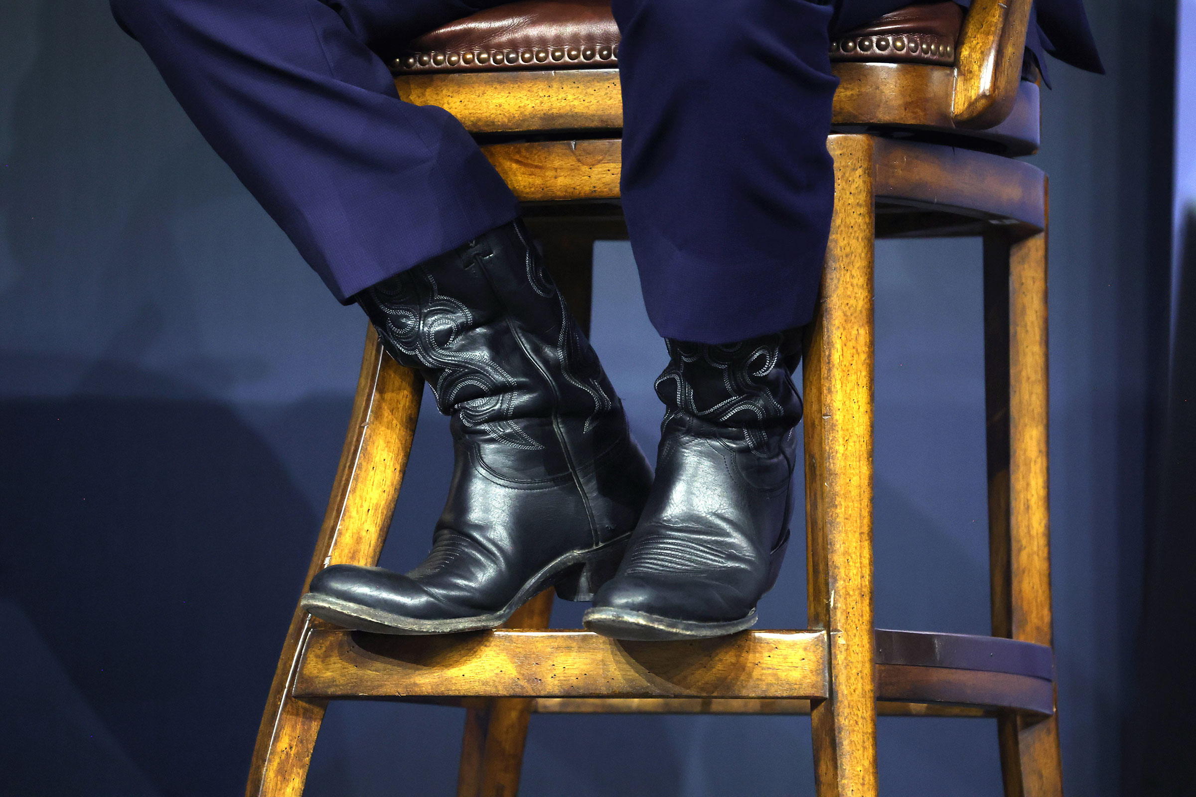A detail image of cowboy boots propped up on a wooden chair, the boots worn by Ron DeSantis