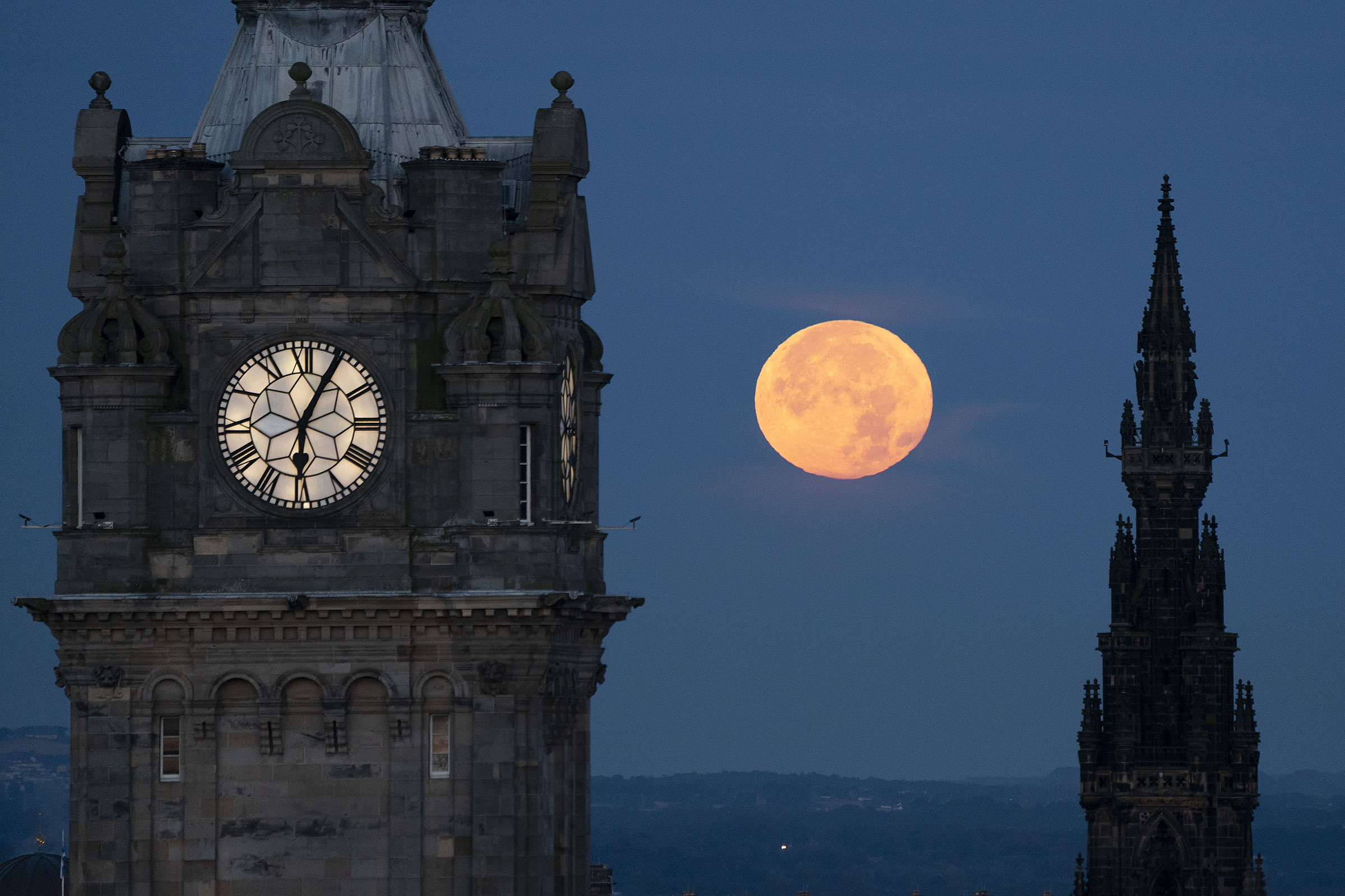 The super blue moon sets between the Balmoral Clock and the Scott Monument in Edinburgh on Aug. 31, 2023.