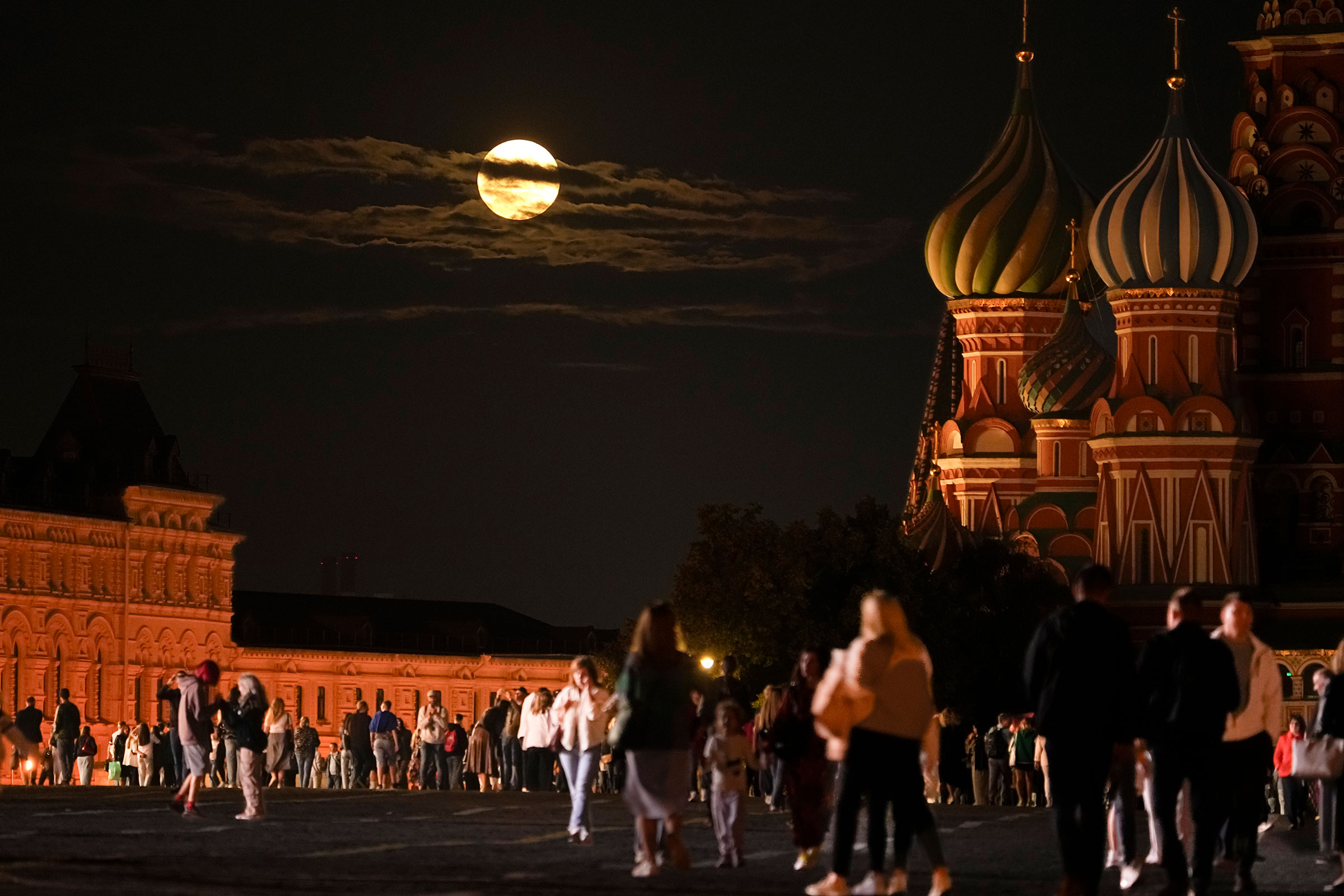 The super blue moon sets behind a historical building and the St. Basil's Cathedral, right, as people walk in Red Square in Moscow, Russia, on Aug. 30, 2023. (Alexander Zemlianichenko—AP)