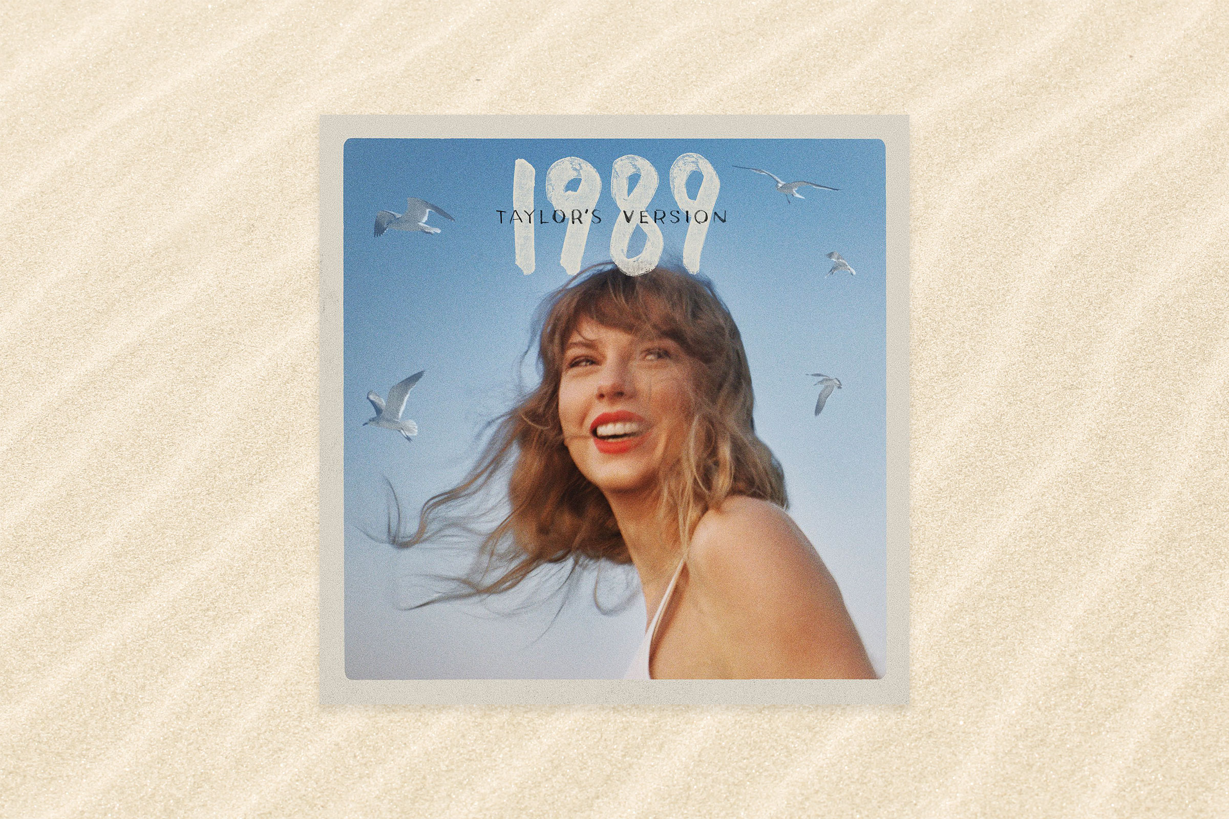 The album cover for 1989 Taylor's Version that shows Taylor Swift smiling with windblown hair with blue sky and birds flying behind her