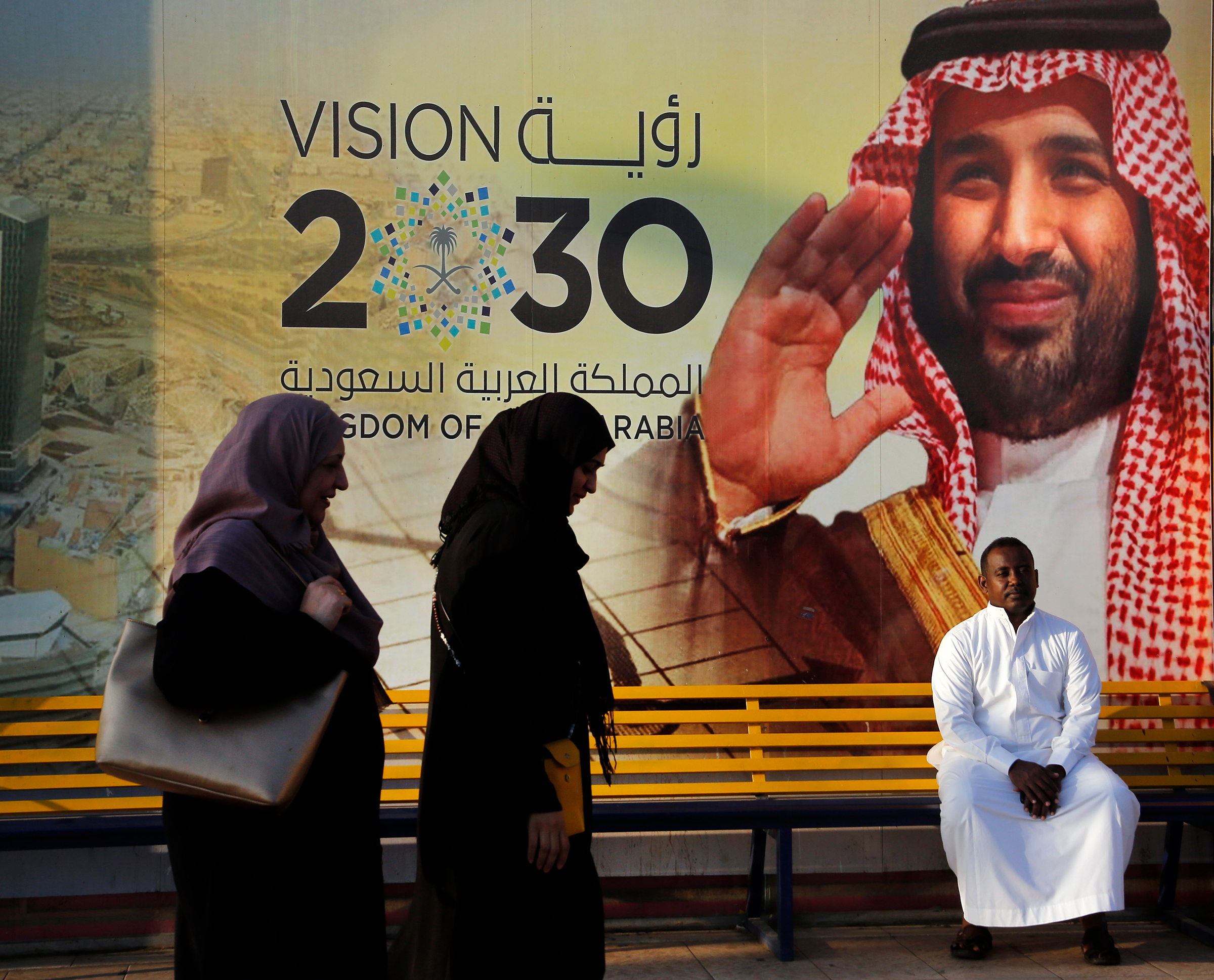 People walk past a banner showing Saudi Crown Prince Mohammed bin Salman, outside a mall in Jeddah, Saudi Arabia, on Dec. 6, 2019. Arabic reads, "vision of 2030". (Amr Nabil—AP)