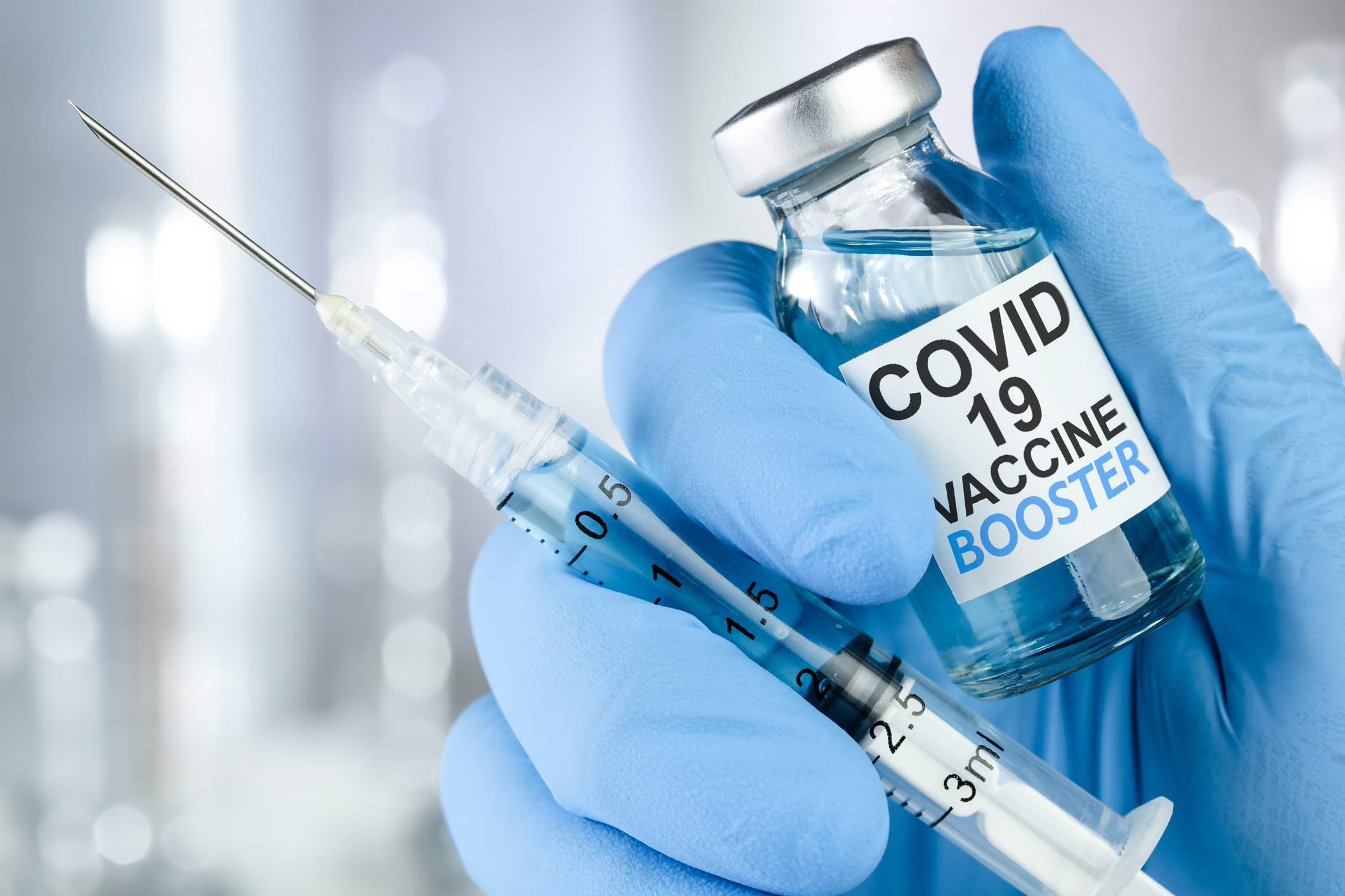 Hand in blue medical gloves holding a syringe and vaccine vial with Covid 19 Vaccine Booster text, for Coronavirus booster shot.