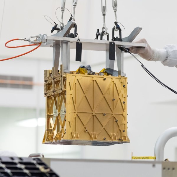 Technicians in the clean room are carefully lowering the Mars Oxygen In-Situ Resource Utilization Experiment (MOXIE) instrument into the belly of the Perseverance rover.