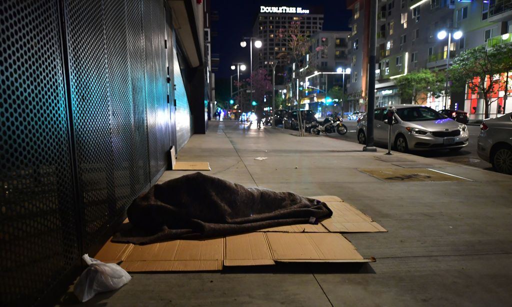 A homeless person sleeps covered with a blanket