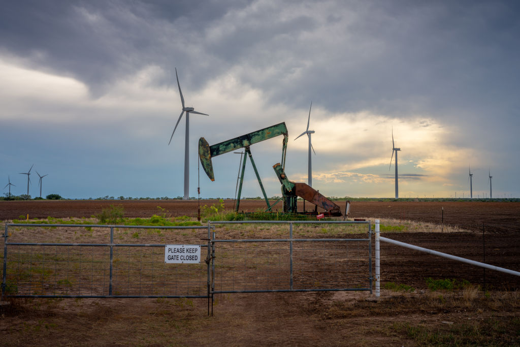 An oil pump jack with with wind turbines in the background