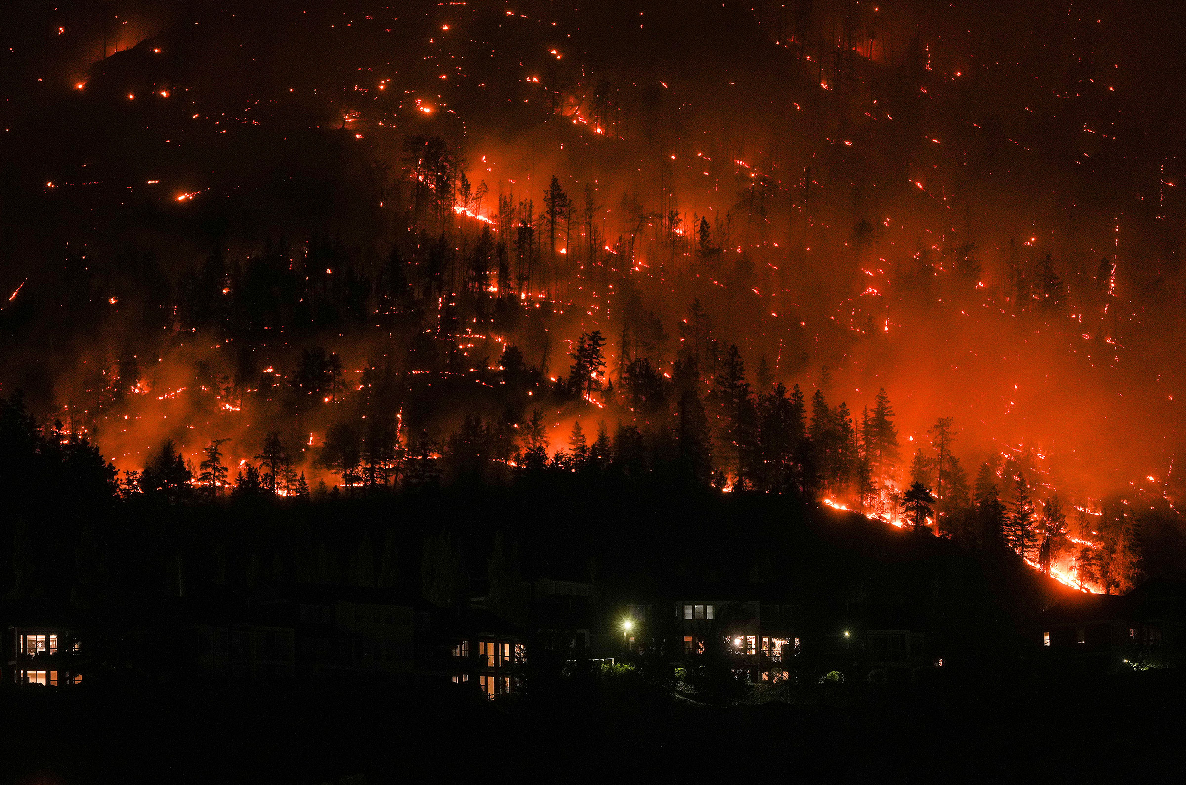 The McDougall Creek wildfire burns on the mountainside above houses in West Kelowna, B.C., on Aug. 18.