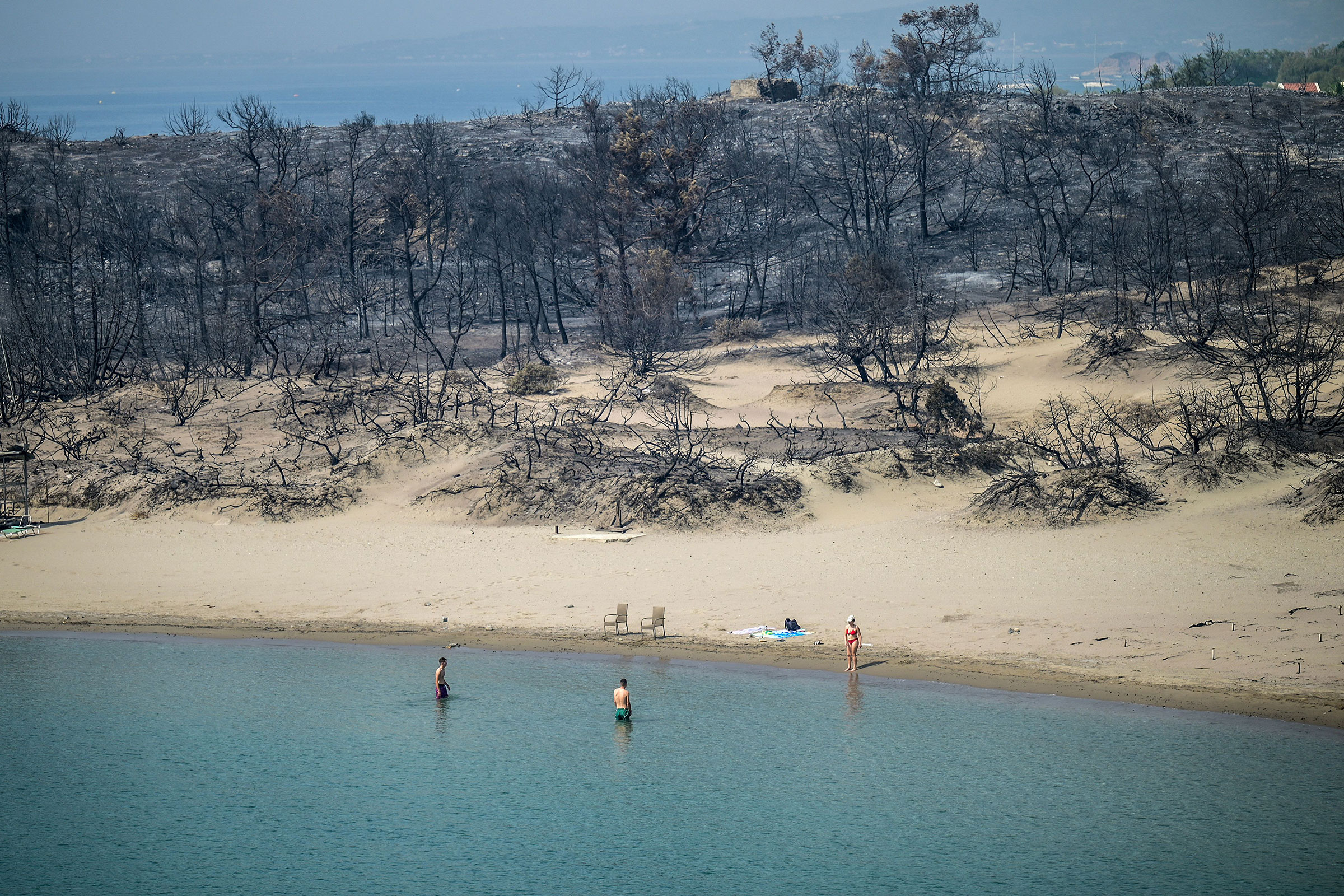 A woman enters the sea from a beach where wildfires destroyed the woods, at Glystra near the village of Gennadi in the southern part of the Greek island of Rhodes, on July 27.
