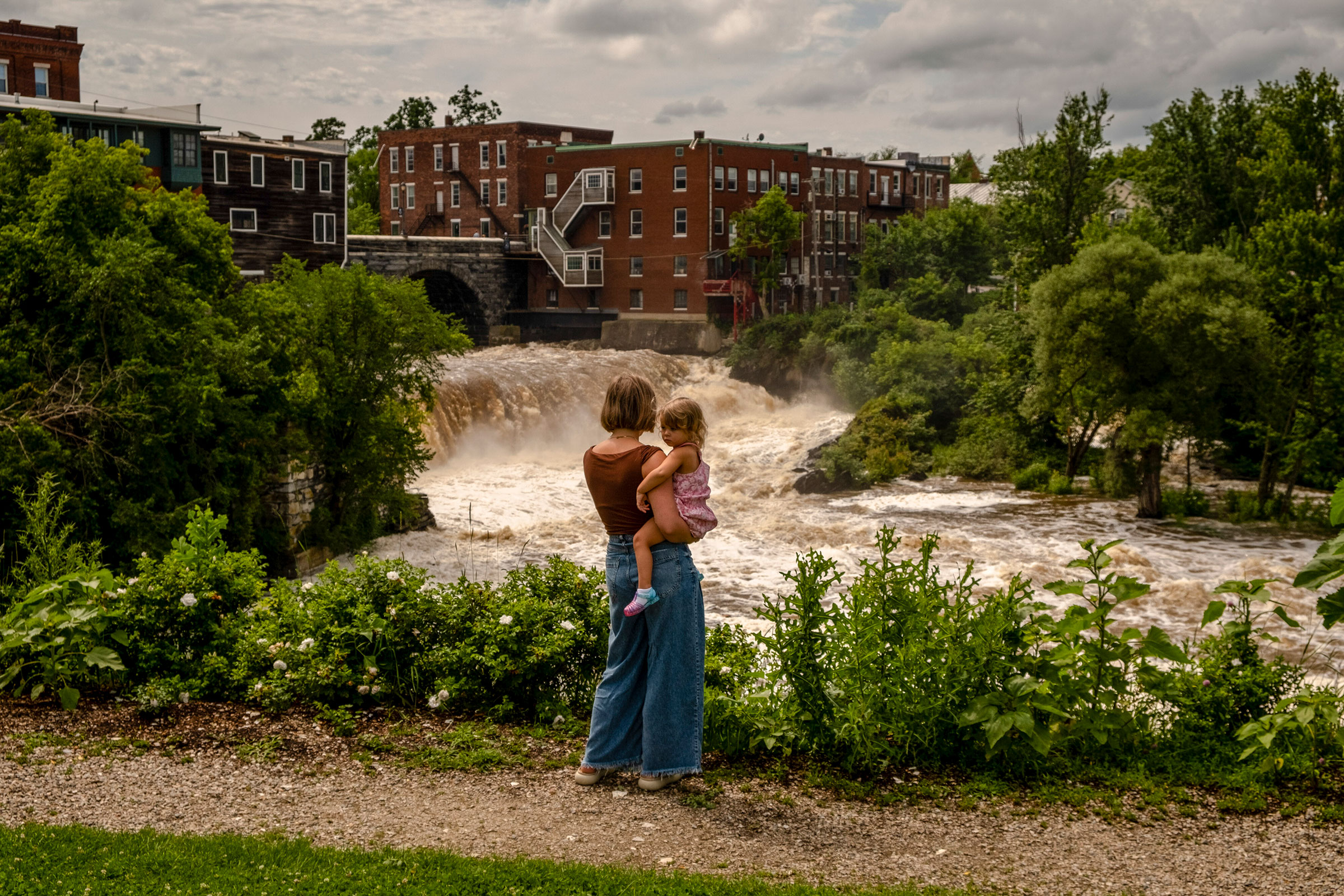 Lauren Rowley and her daughter Ursula, 2, look at the surging Otter Creek River in downtown Middlebury, Vt., on July 14, 2023. Vermont began new flood protection efforts after being battered by Tropical Storm Irene in 2011. Many appeared to be effective, but experts say more will be needed as storms become more extreme.