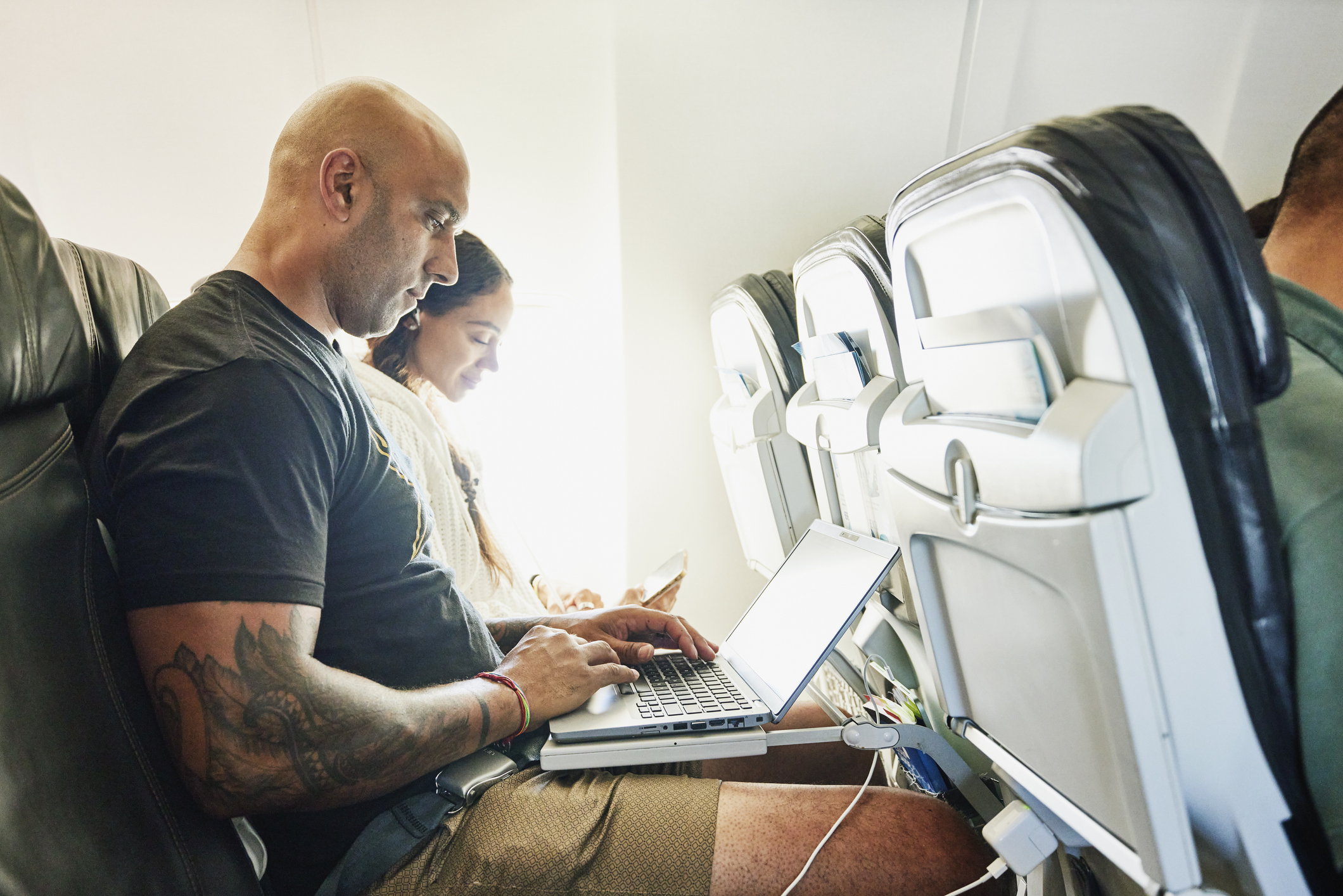 Medium shot of couple working on smart phone and laptop on airplane