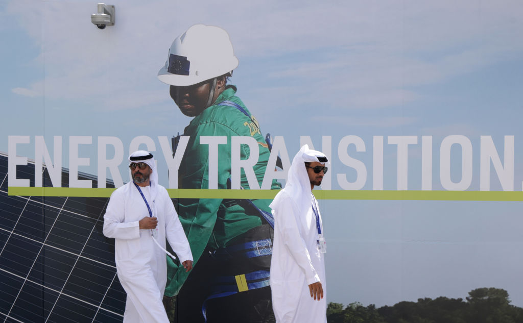 Men wearing thawbs walk past a billboard promoting the transition to renewable energies at the UNFCCC COP28 Climate Conference in Dubai, United Arab Emirates.