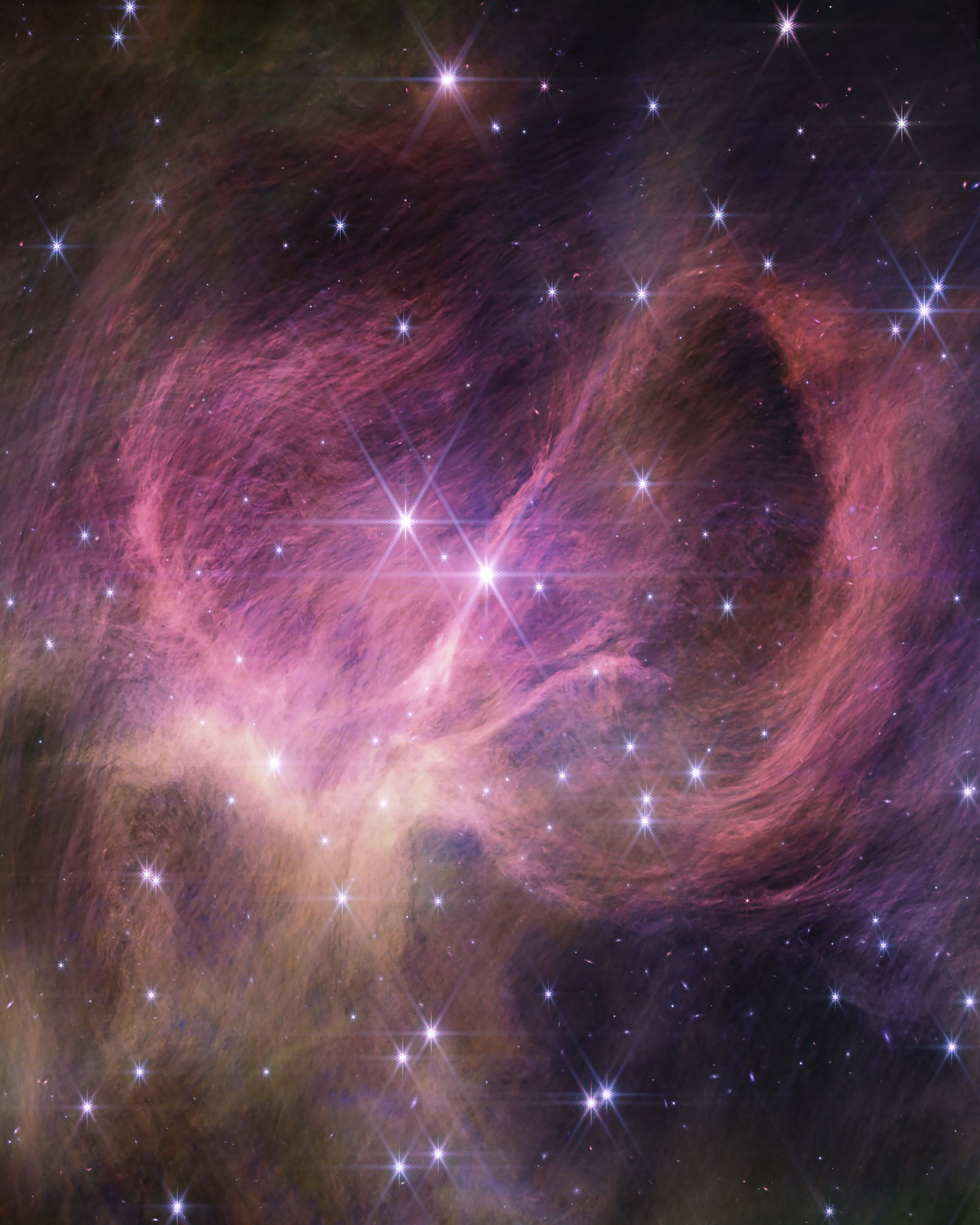 Wispy hair-like filaments of pink-purple fill the middle of the image, curving left and right on either side of the center. On the right, the filaments form a dramatic loop that seems to extend toward the viewer. At lower left are additional yellowsish filaments. Two prominent, bright stars near the center of the image show Webb’s eight-point diffraction spikes. Dozens of fainter stars are scattered across the image.