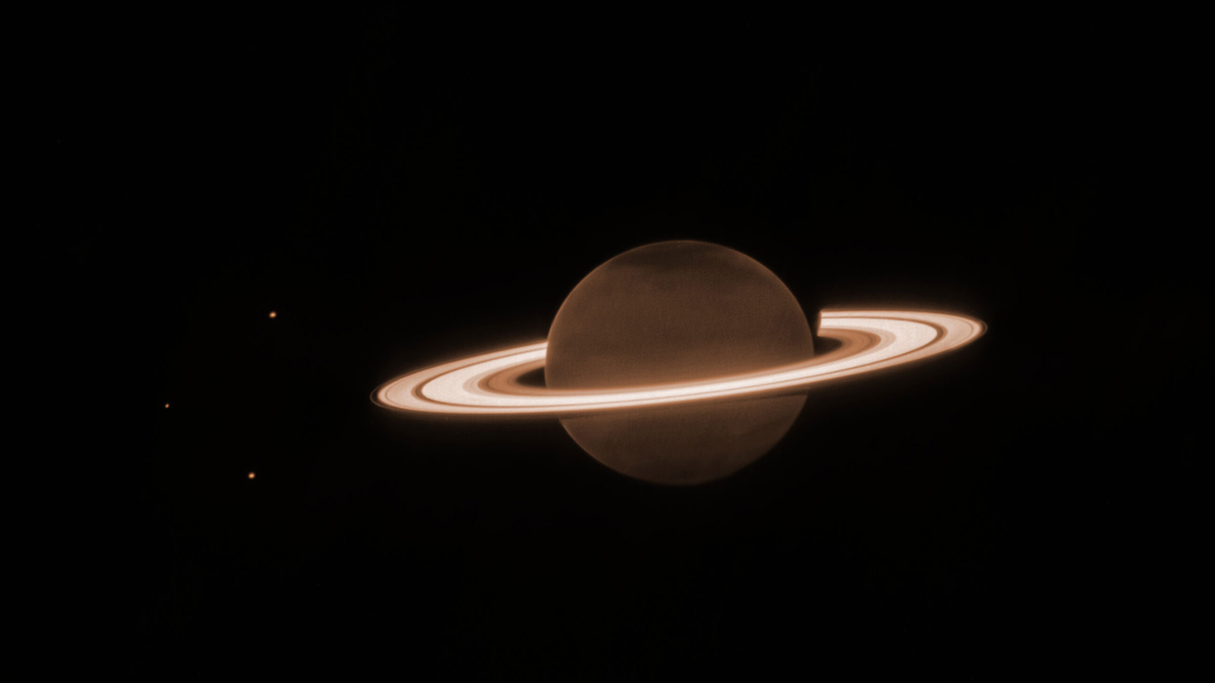 O fundo é quase todo escuro.  No centro há um círculo marrom-alaranjado escuro, cercado por vários anéis horizontais esbranquiçados, grossos e brilhantes.  Este é Saturno e seus anéis.  Existem três pequenos pontos na imagem – um no canto superior esquerdo do planeta, um diretamente à esquerda do planeta e no canto inferior esquerdo do planeta.  Estas são três luas de Saturno: Dione, Encélado e Tétis, respectivamente.  Há uma tonalidade ligeiramente mais escura nos pólos norte e sul do planeta.  Os anéis que circundam Saturno são em sua maioria largos, com algumas lacunas estreitas e singulares entre os anéis mais largos.  Há um anel mais interno e mais grosso e, próximo a ele, um anel mais brilhante e mais largo.  Viajando mais para fora, há uma pequena lacuna escura antes de outro anel mais espesso.  No anel mais grosso, há uma faixa estreita e fraca.  Existe então um anel mais externo, mais fraco e mais fino.