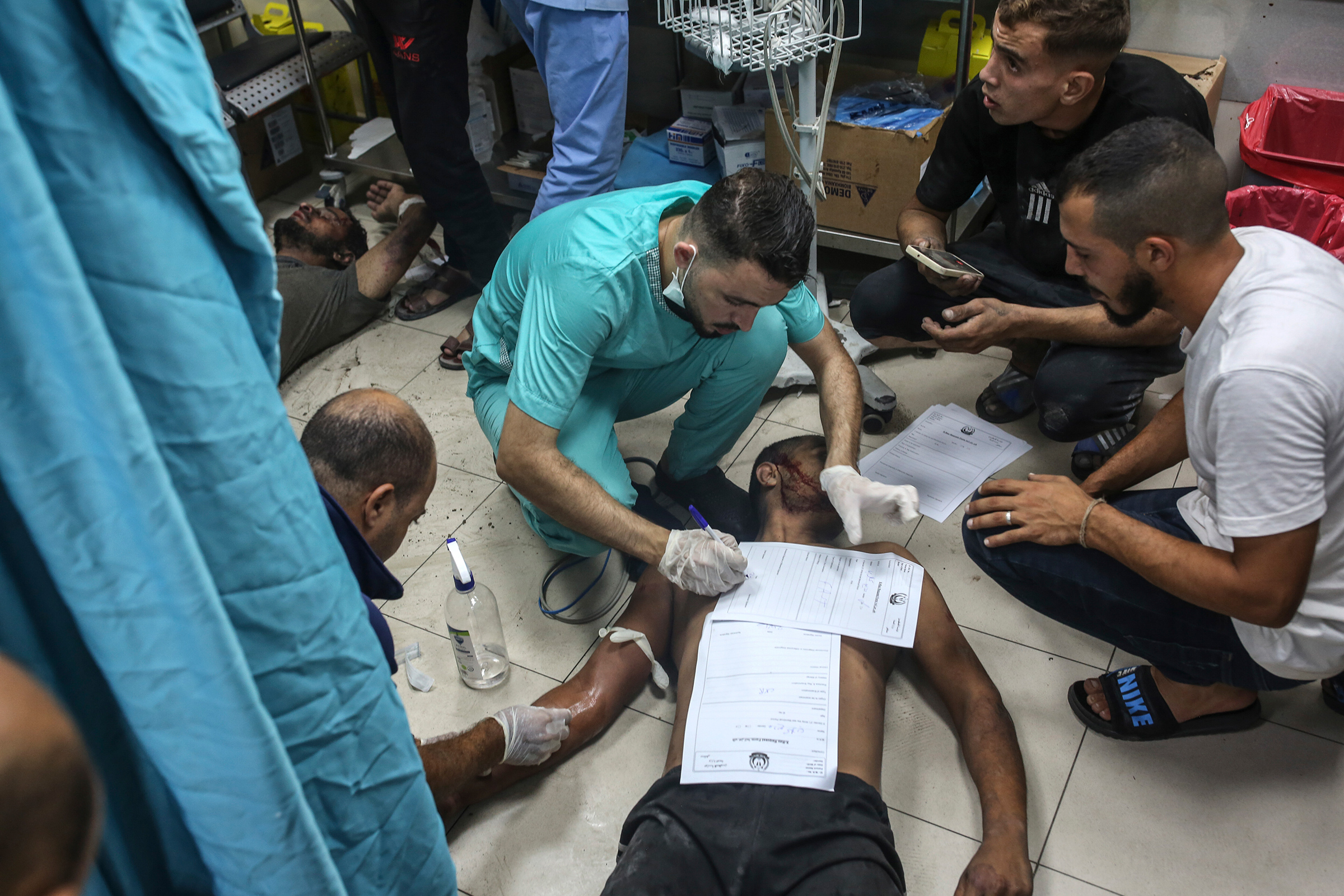 A doctor fills out paperwork on top of a patient on the floor at Nasser Medical Hospital in Khan Younis, in the southern Gaza Strip, on Oct. 24.