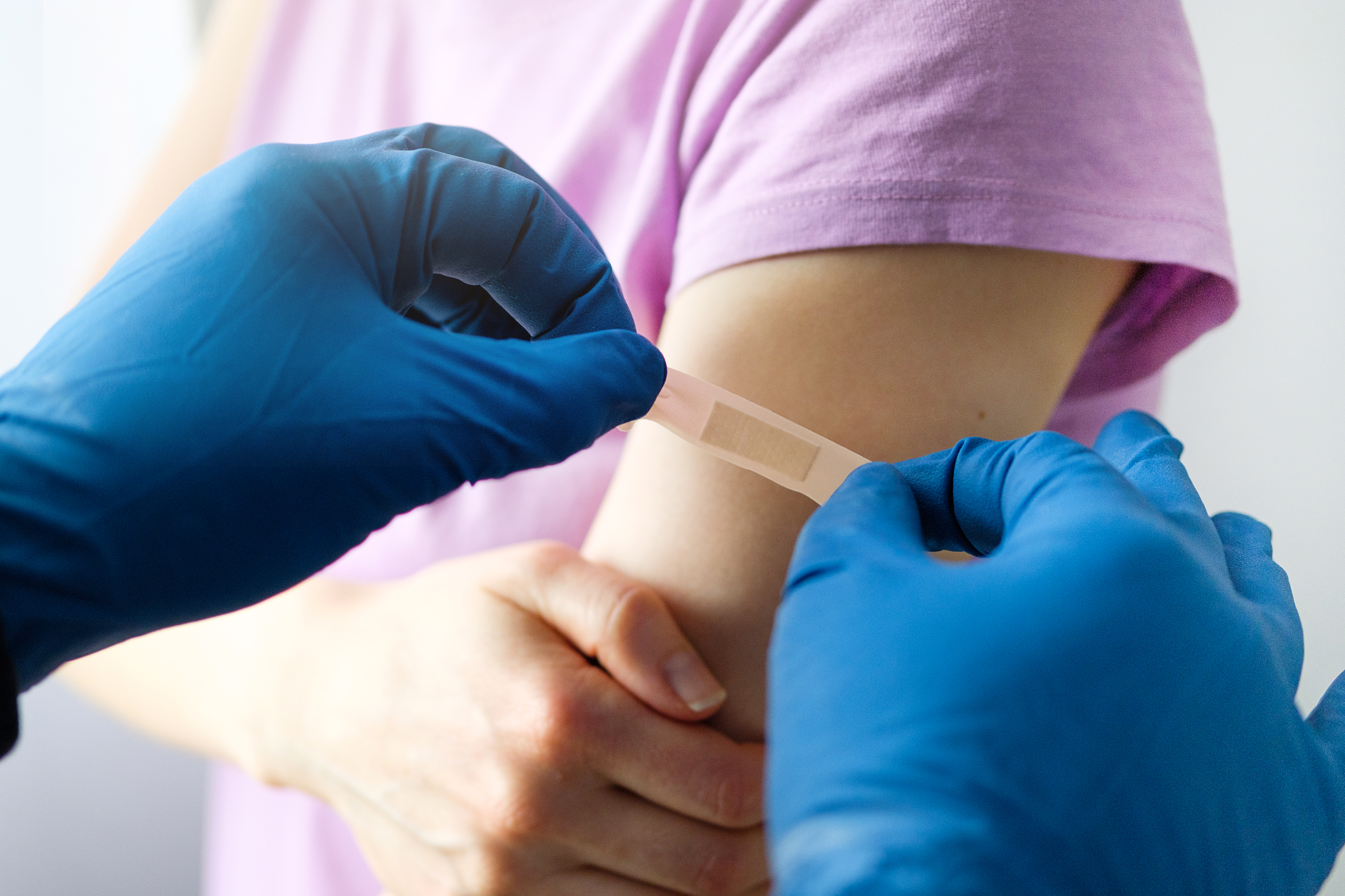 A gloved doctor or health care professional applies a patch or adhesive bandage to a girl or young woman after vaccination or drug injection. The concept of medicine and health care, vaccination and treatment of diseases. First aid services.