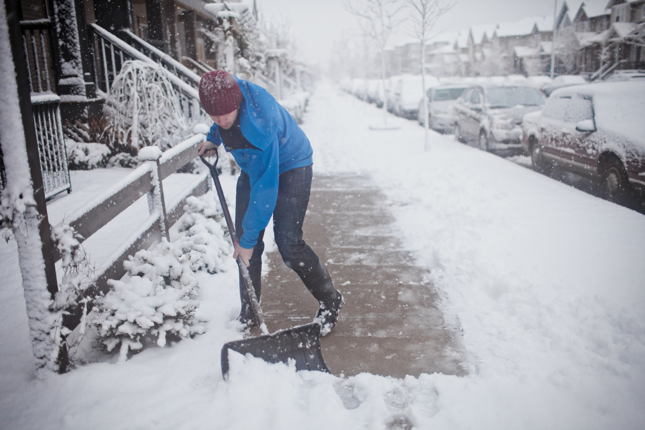 A man shovels the sidewalk outside of his suburban house.