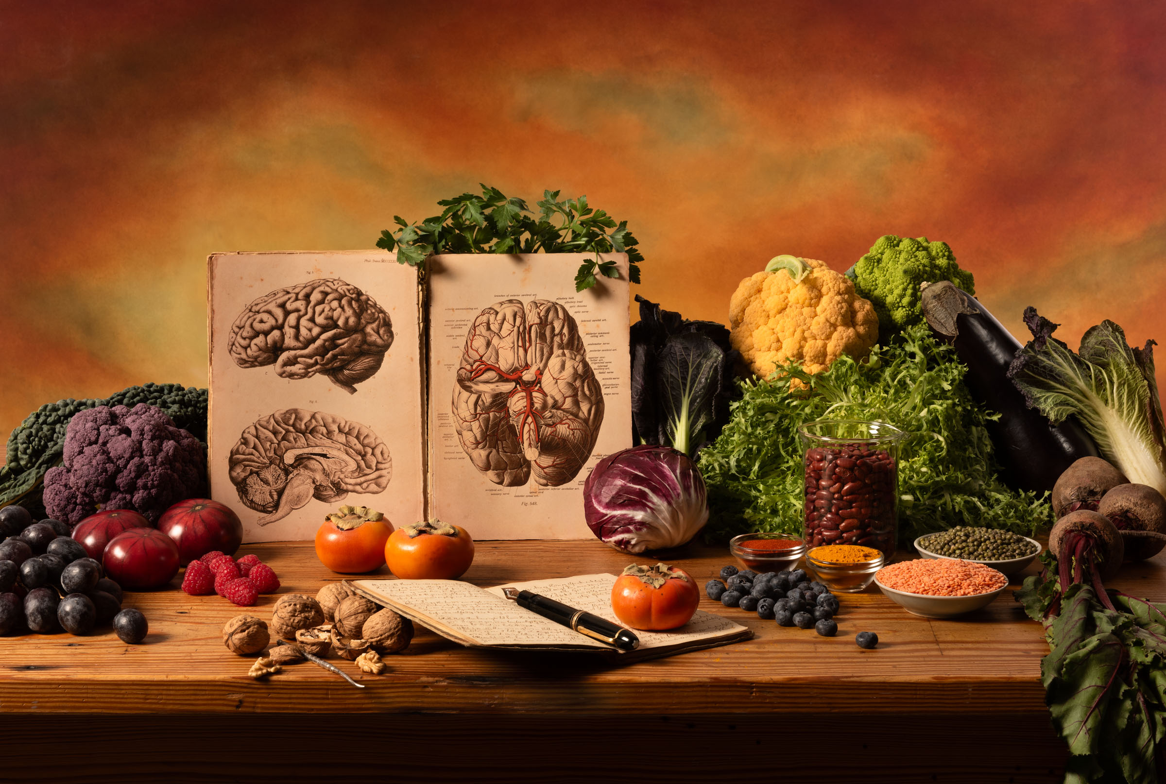 An abundance of vegetables on a table next to an anatomy drawing of a brain.