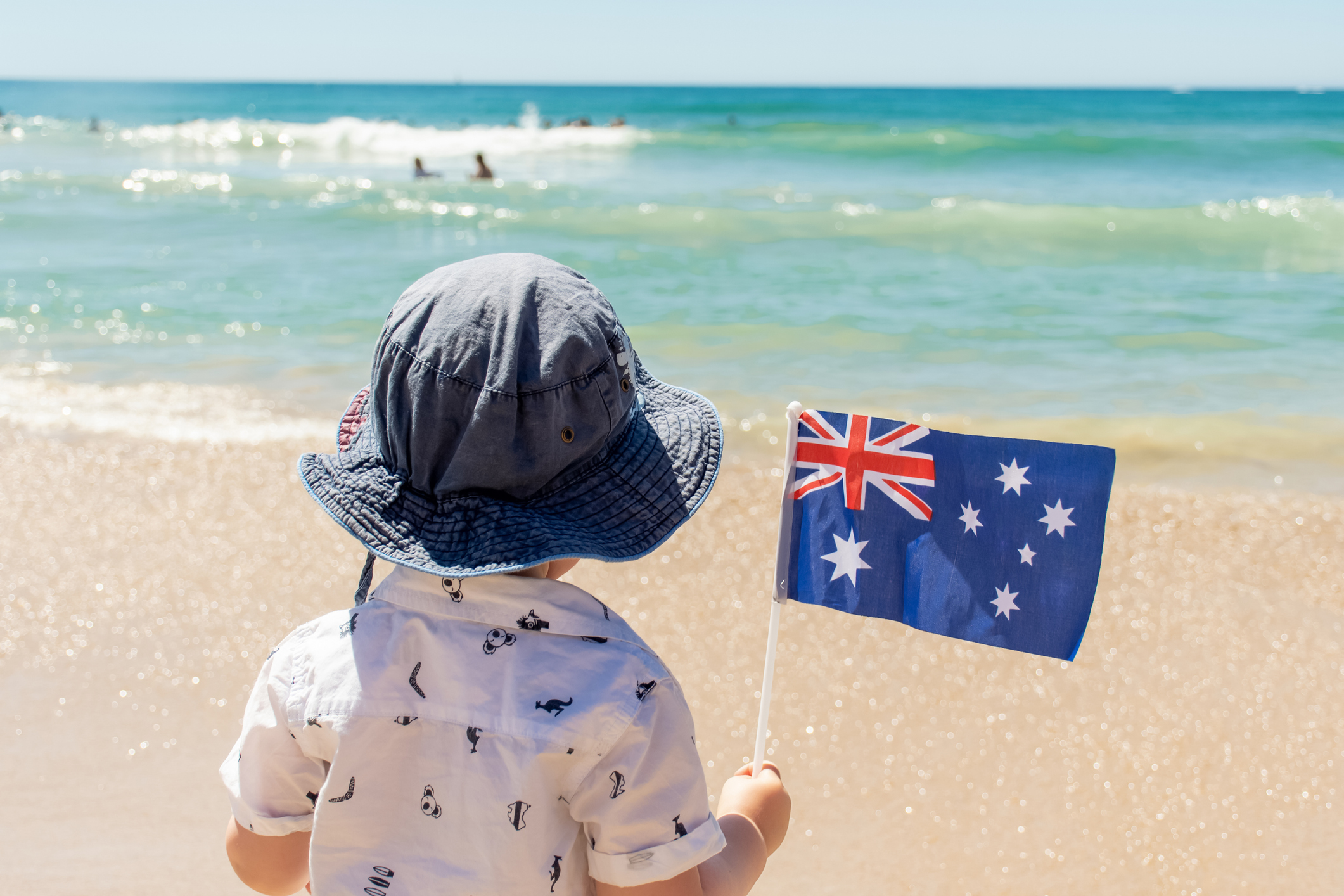 Little boy wearing hat holding Australian flag on a sandy ocean beach. Australia Day concept