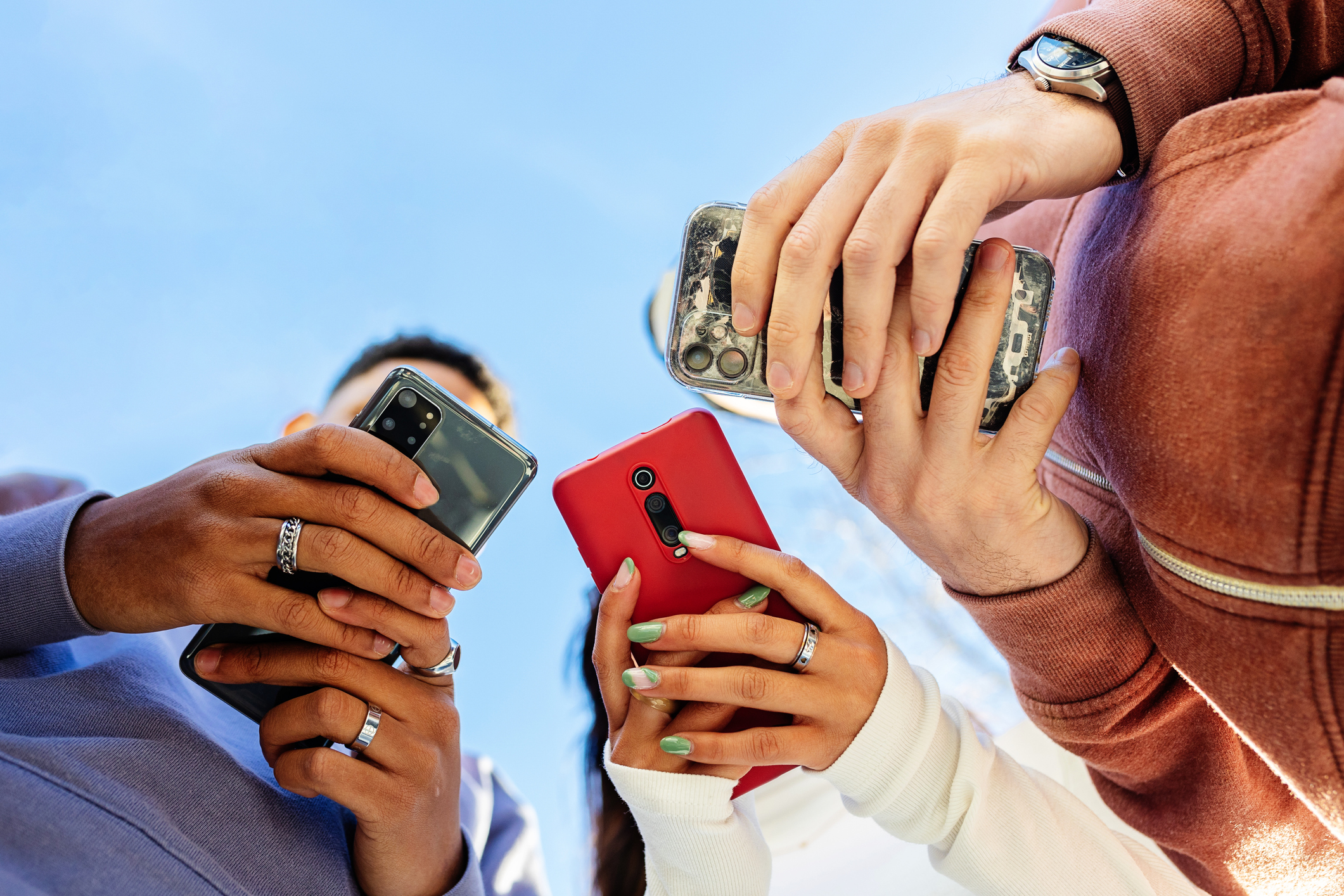 Low angle view of three young people using mobile phones outdoors