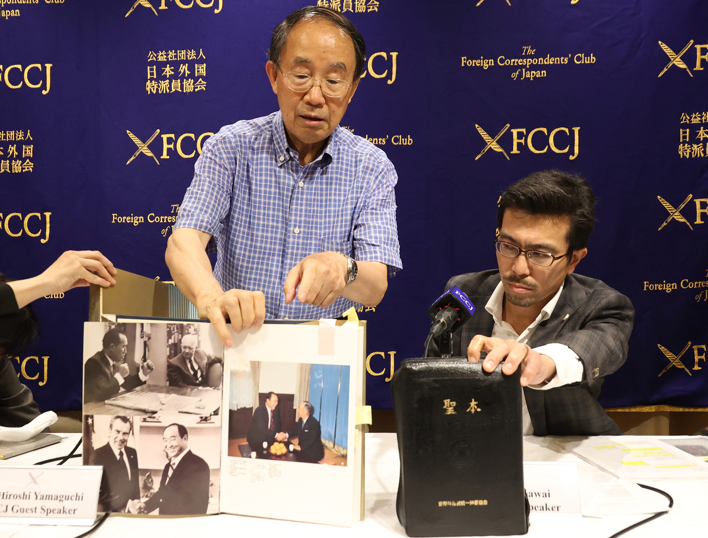 Members of the National Network of Lawyers Against Spiritual Sales, Hiroshi Yamaguchi, left, and Yasuo Kawai, right, display a history book of the Unification Church and the cult's Holy book at a press conference about activities of the Unification Church at the Foreign Correspondents' Club of Japan in Tokyo on July 29, 2022.