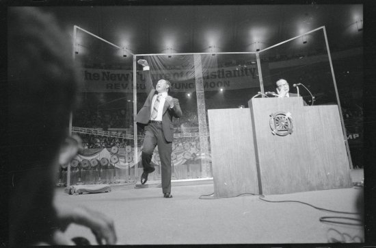 The Reverend Sun Myung Moon, Korean evangelist, gestures dramatically as he speaks at New York's Madison Square Garden. His chief associate, Col. Bo Hi Park, (right) translates the evangelist's Korean to English. The Reverend Moon said that God had told him to bring his message to America.