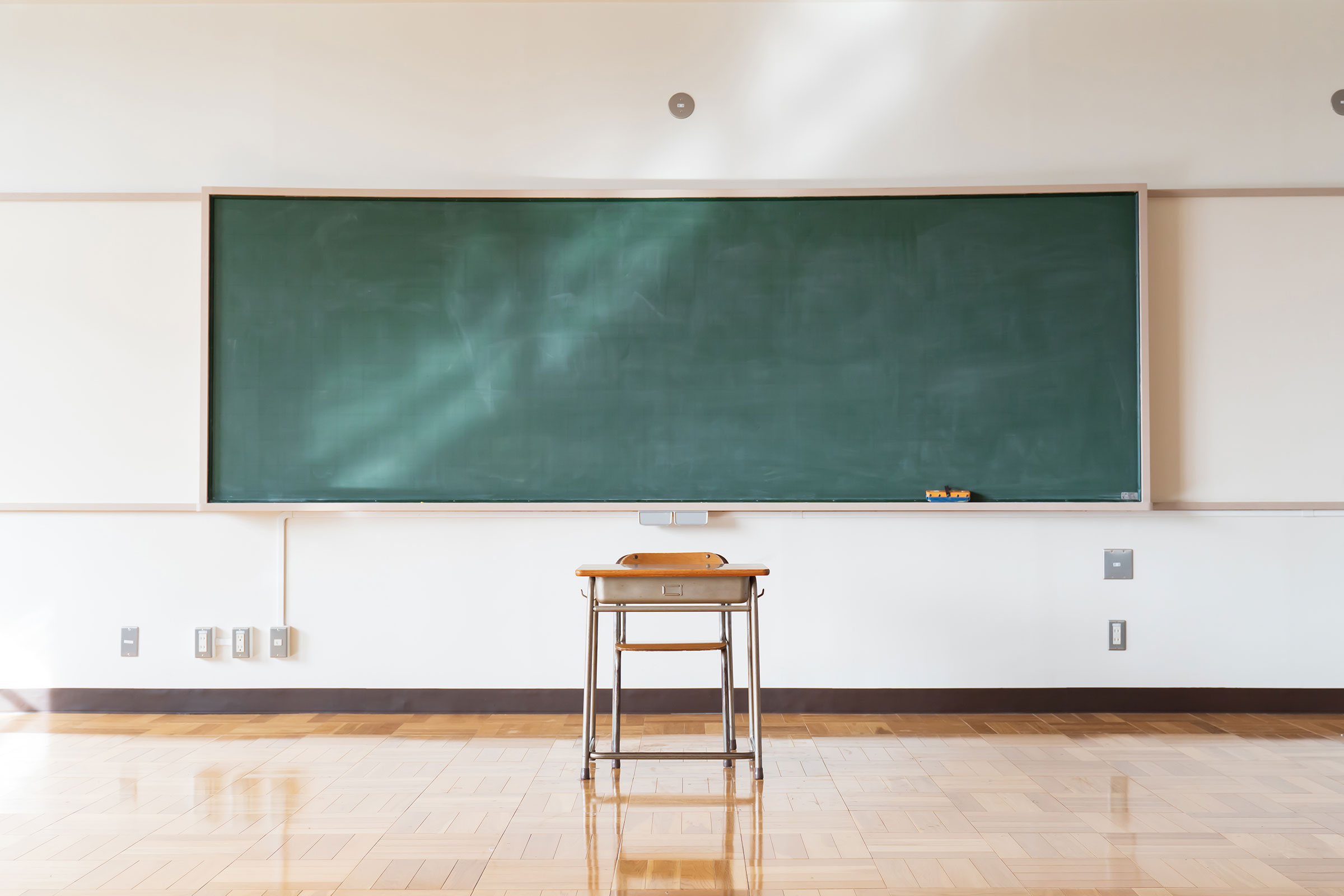 A single desk sitting in front of a blackboard in a classroom