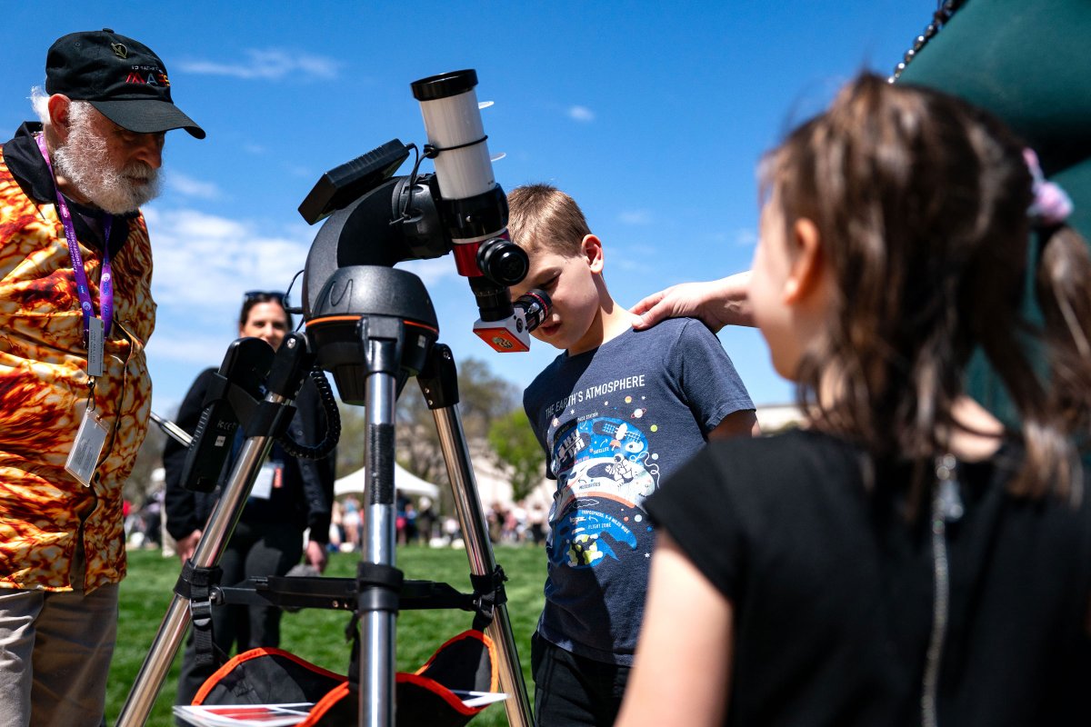 People look through a telescope that is tracking the path of the sun as people gather on the National Mall in Washington, D.C., to view the partial solar eclipse.