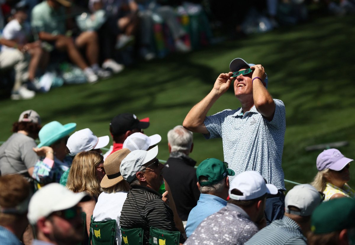 A man stands to watch the eclipse during a practice round at The Masters, in Augusta, Ga.