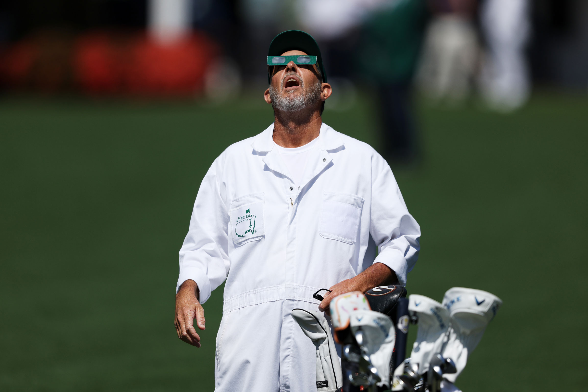 A caddie uses glasses to view the eclipse during a practice round prior to the 2024 Masters Tournament