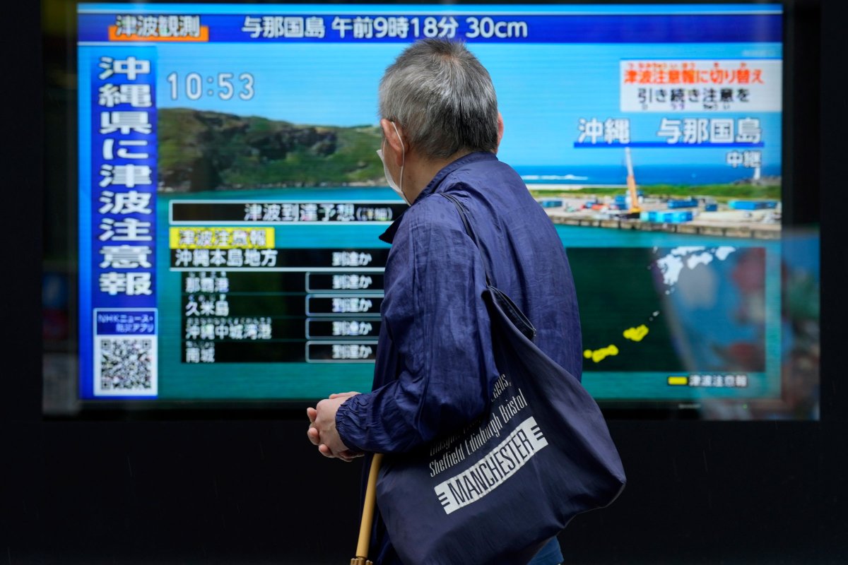 A person stands along a sidewalk to watch a TV showing a breaking news on tsunami for Okinawa