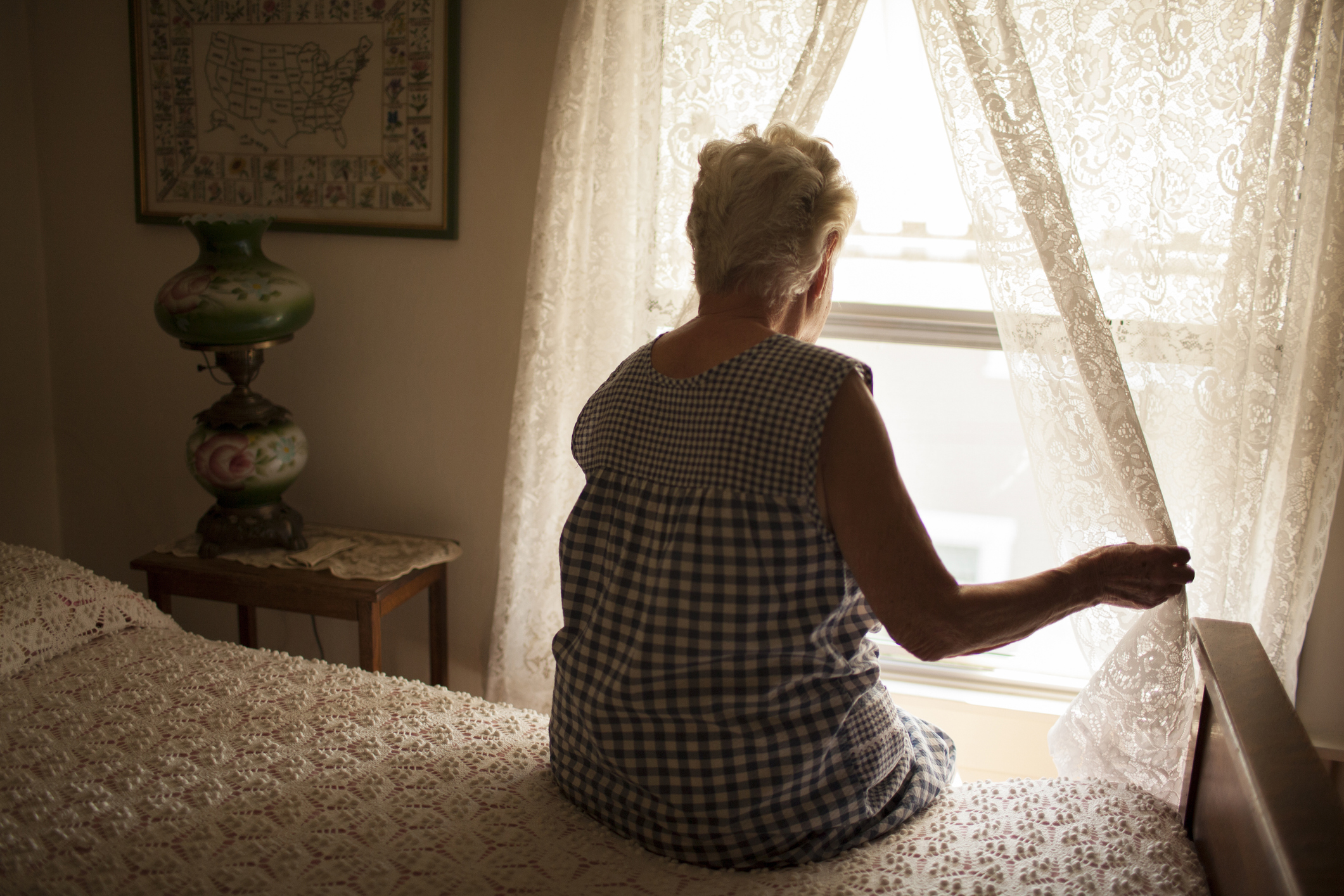 Pensive older woman looking out bedroom window